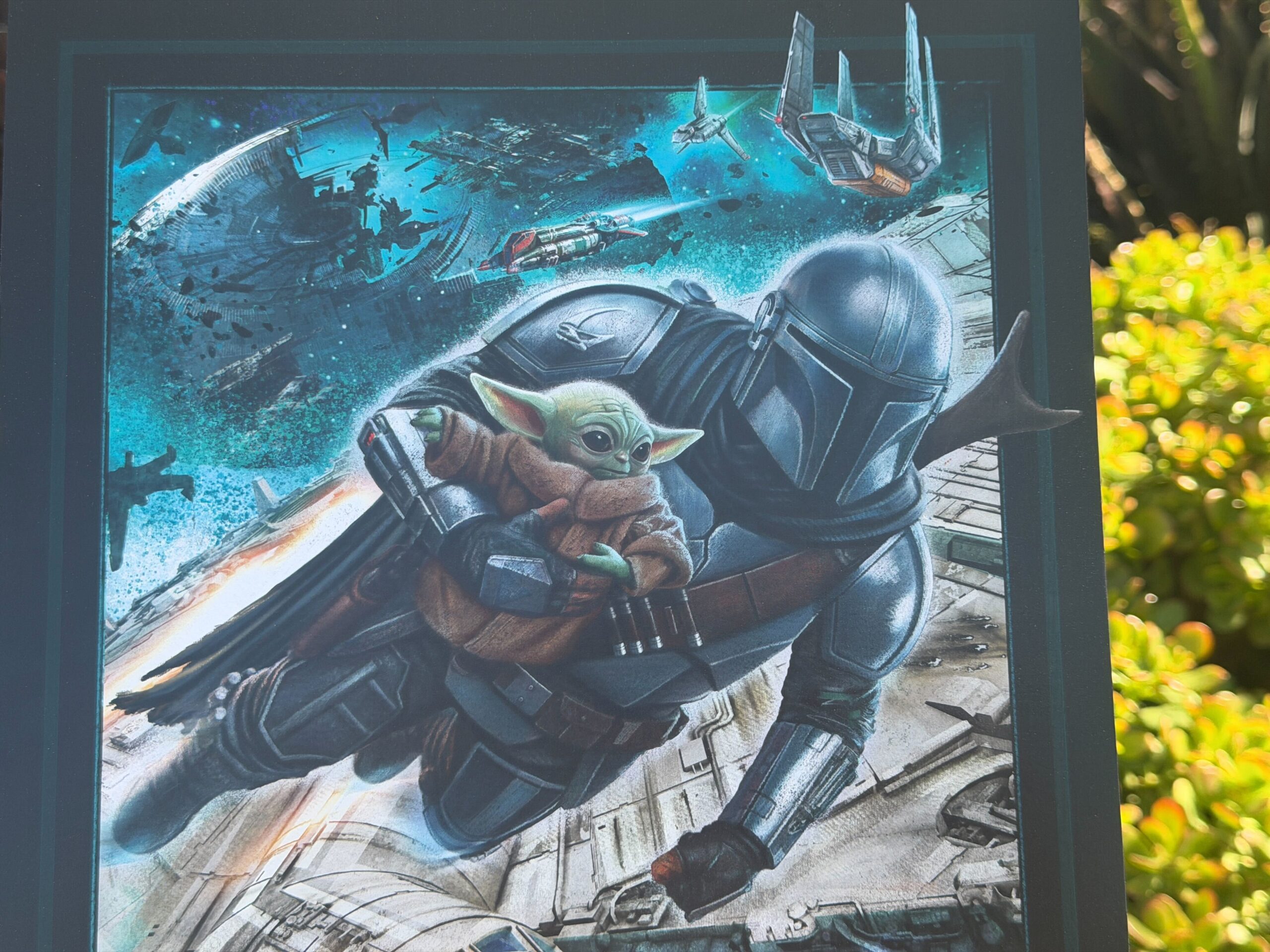 The attraction poster is reminiscent of the first concept art Disney shared but viewed from outside the Millennium Falcon rather than inside. Mando holds Grogu as he flies alongside the ship above Batuu. A TIE Fighter and a yellow ST-70 assault ship similar to Mando’s old Razor Crest fly nearby. In the sky above are the ruins of the Death Star, an Imperial shuttle, and an Imperial landing craft.