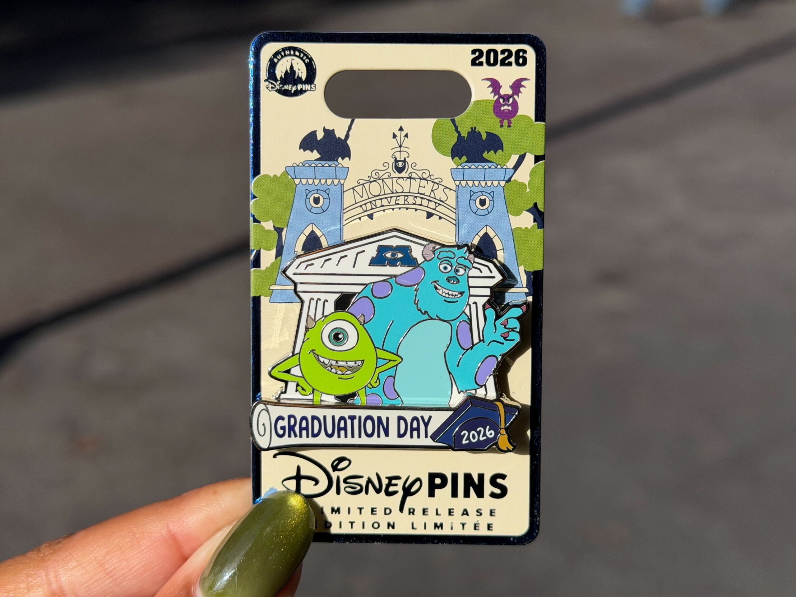 Mark graduation with this pin featuring Mike and Sulley in front of a Monsters University building. A scroll at the bottom reads "Graduation Day" with "2026" on a graduation cap.
