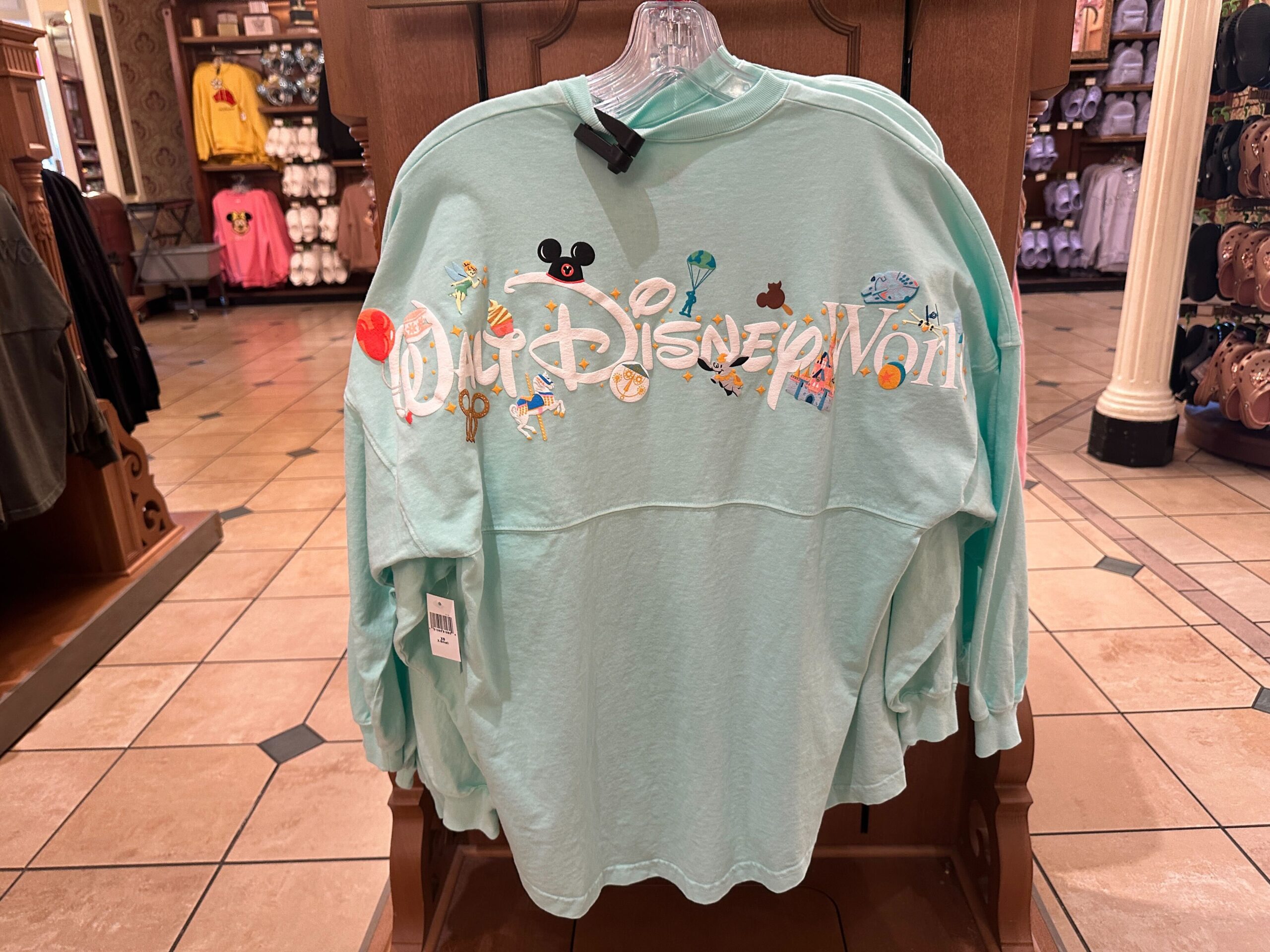 On the back of the Spirit Jersey is the Walt Disney World wordmark in white surrounded by park iconography. Some of the icons seen on it include a DOLE Whip, Dumbo, Cinderella Castle, a carousel horse, and more.