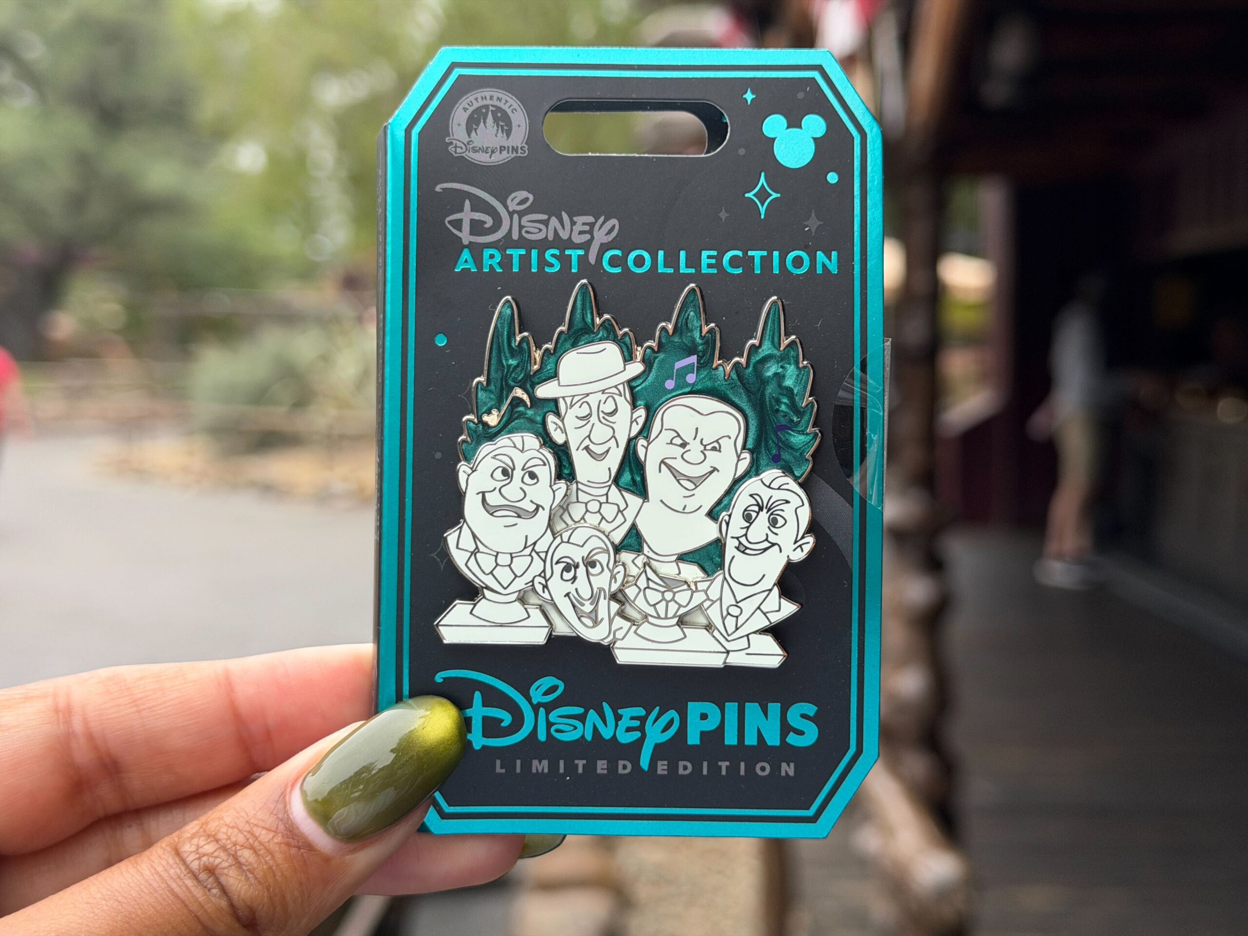 The singing busts from The Haunted Mansion are pictured in this pin-on-pin design. The marbleized background resembles green shrubbery with some music notes.