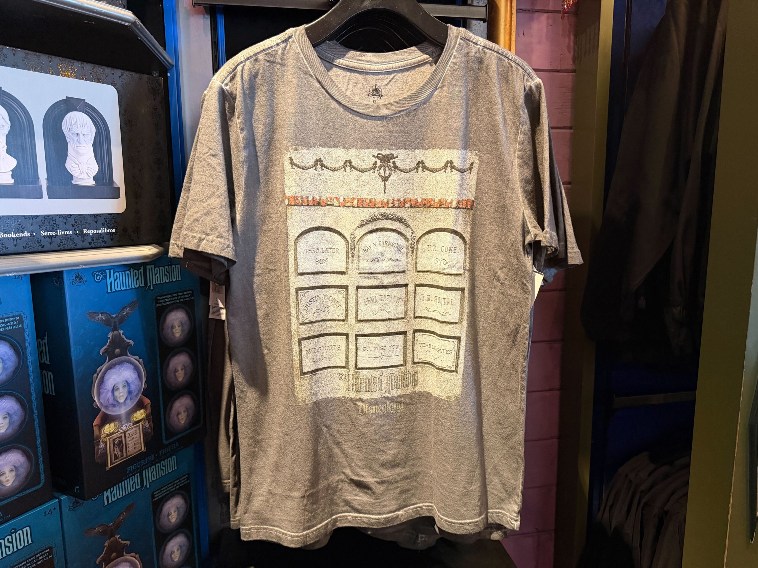 This grey t-shirt has a large graphic on the front, which shows The Haunted Mansion wordmark at the bottom above the Disneyland Resort wordmark. Decorations from the attraction are seen adorning the top of the graphic.