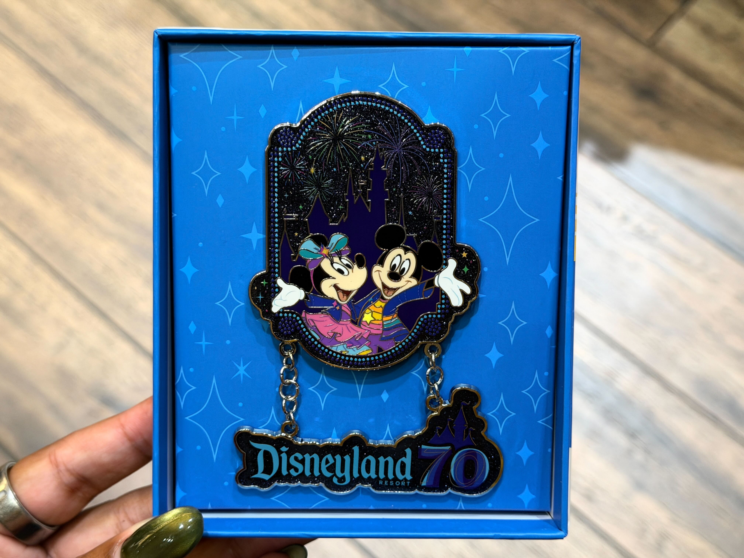 Similar to the pin above, this one shows Minnie and Mickey in their anniversary outfits in front of Sleeping Beauty Castle with fireworks in the sky. A hanging "Disneyland 70" charm is below them.