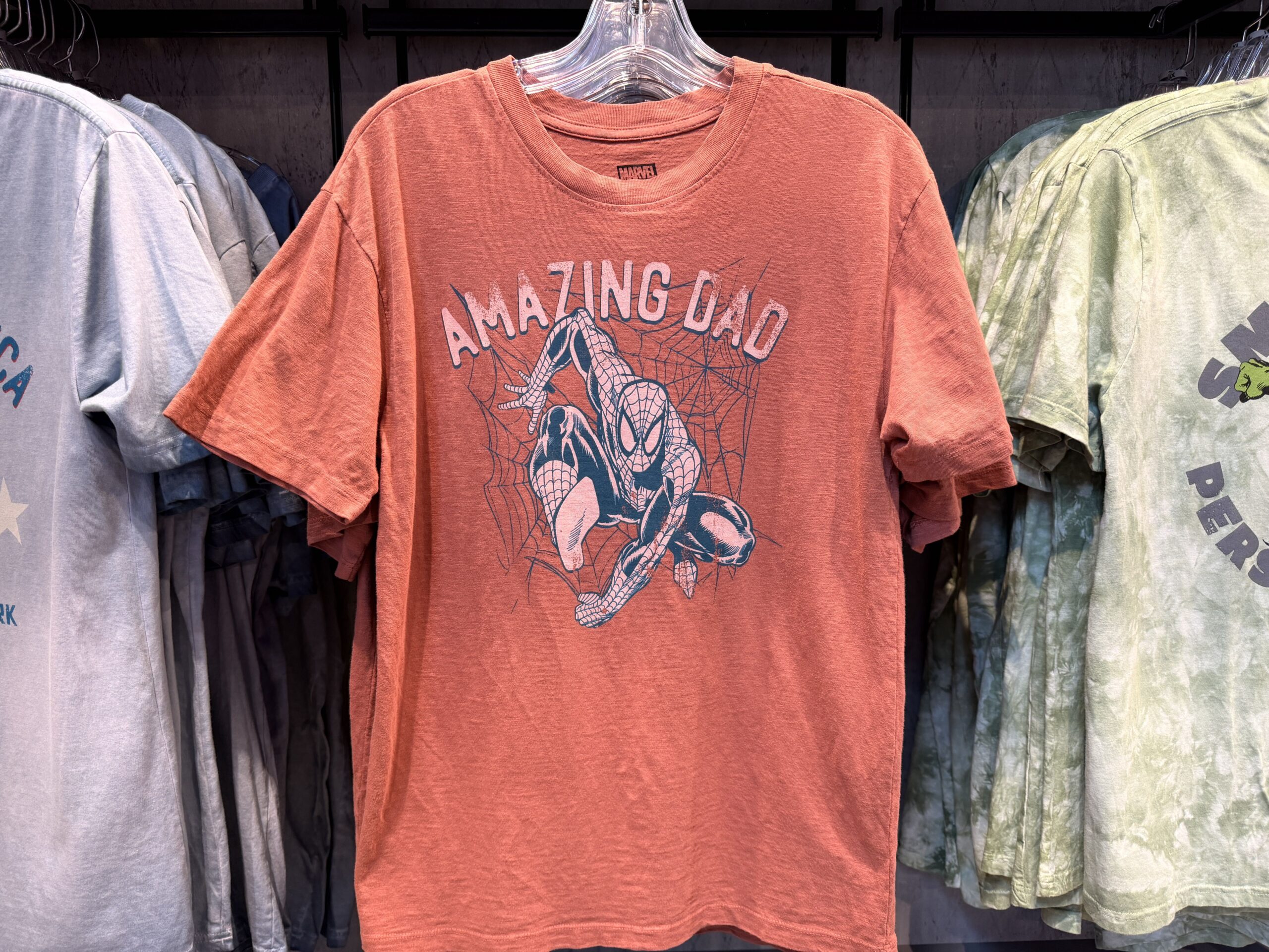 This muted red shirt features blue artwork of Spider-Man jumping from a web. "Amazing Dad" is in faded white lettering.