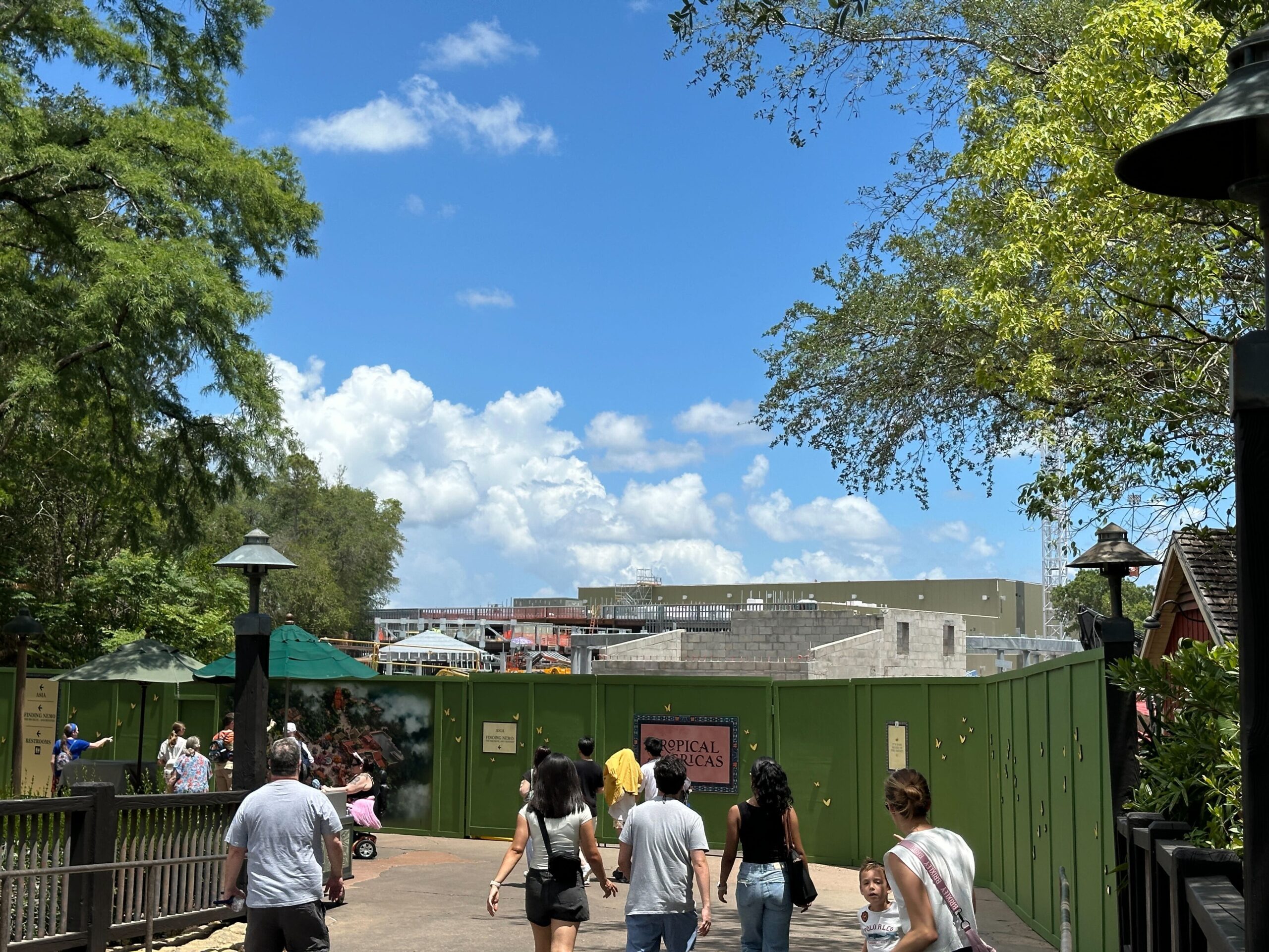 Meanwhile, construction continues to progress on the Encanto ride building, with a mix of cinder block and steel walls visible behind the green construction walls.