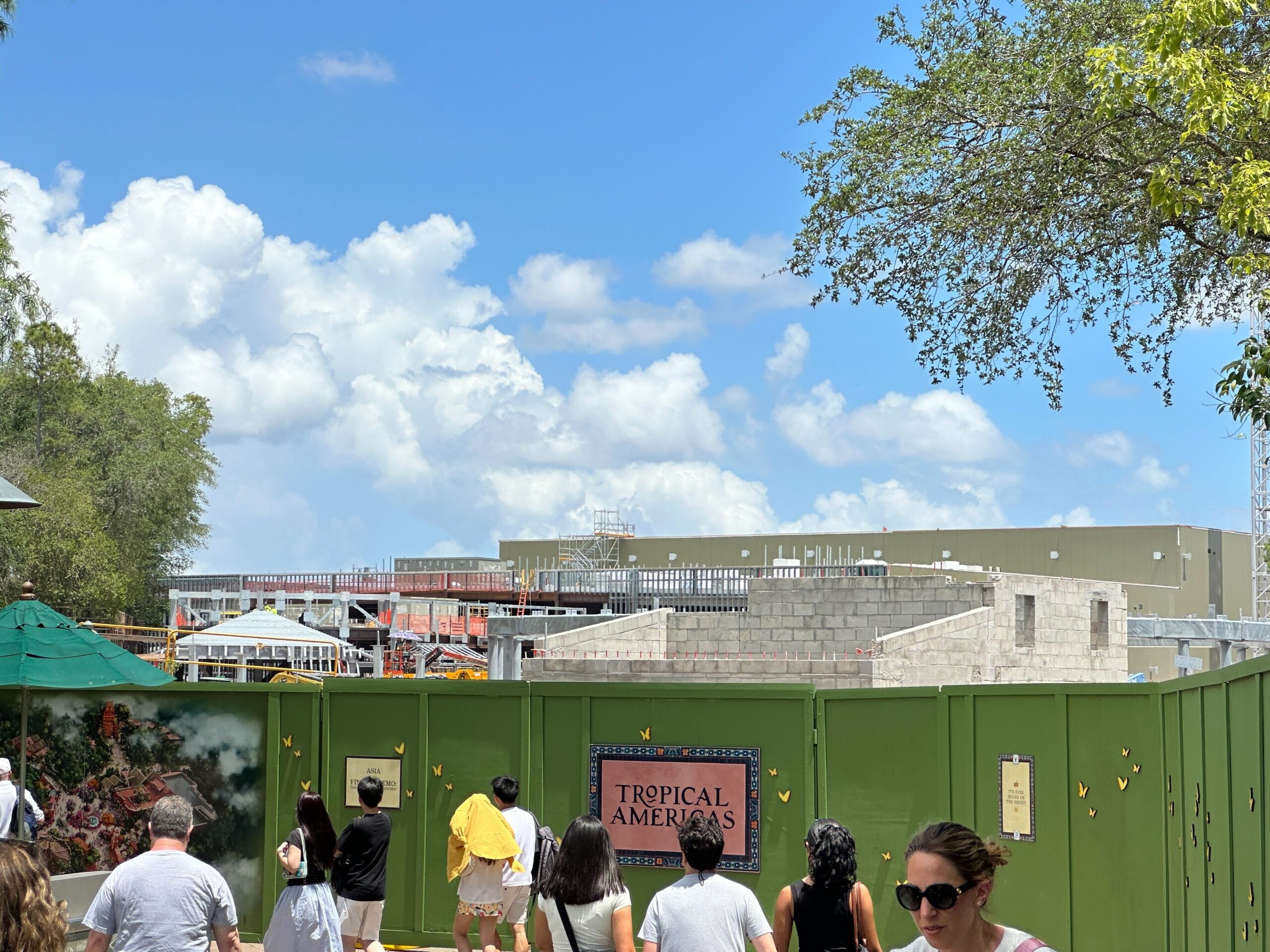 Meanwhile, construction continues to progress on the Encanto ride building, with a mix of cinder block and steel walls visible behind the green construction walls.