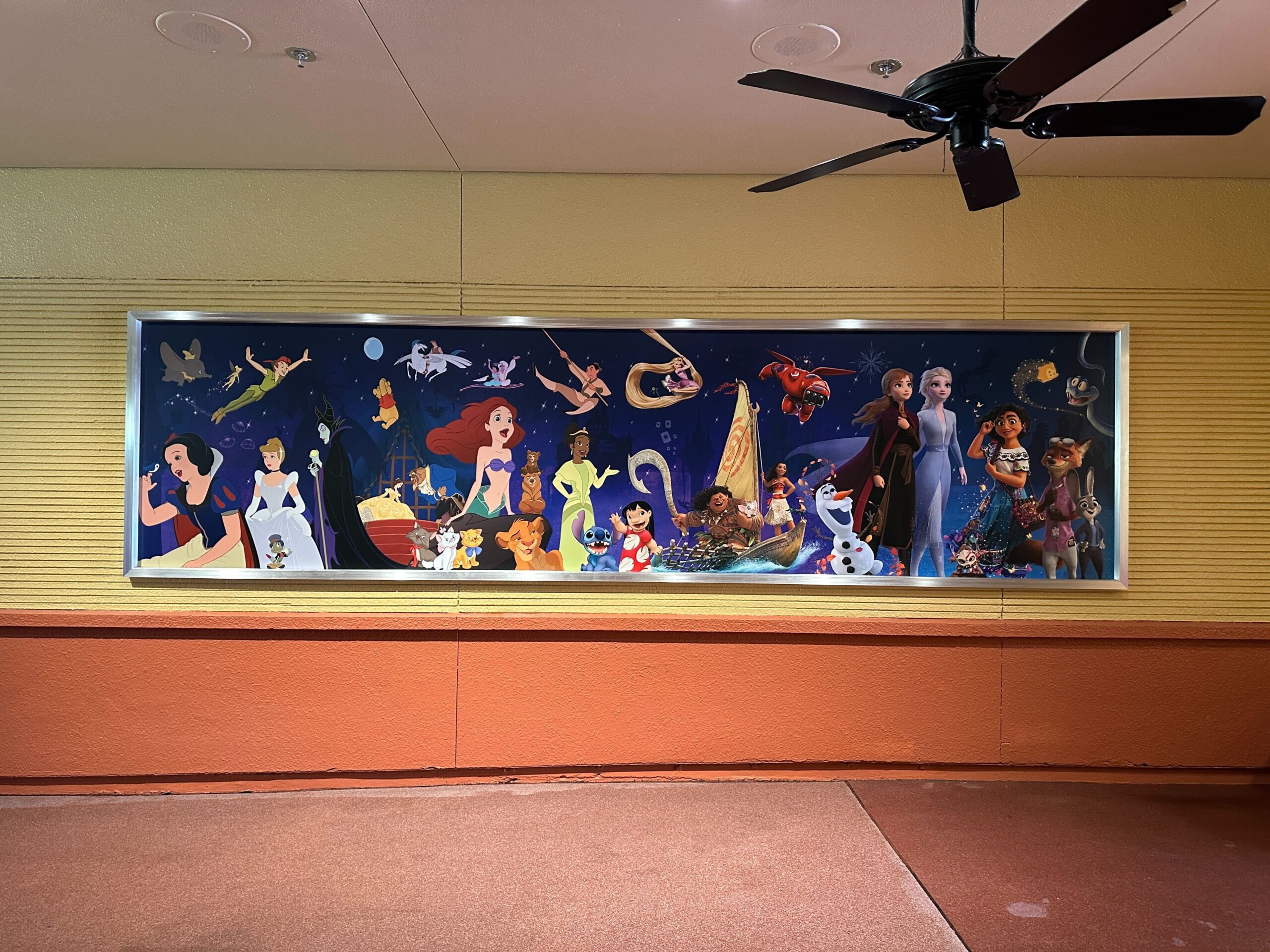 A large mural of Disney characters lines ones of the walls featuring movies like Zootopia, Encanto, Frozen, Big Hero 6, Moana, Tangled, Mulan, Aladdin, Hercules, Beauty and the Beast, Aristocats, Cinderella, Peter Pan, Snow White and many more.