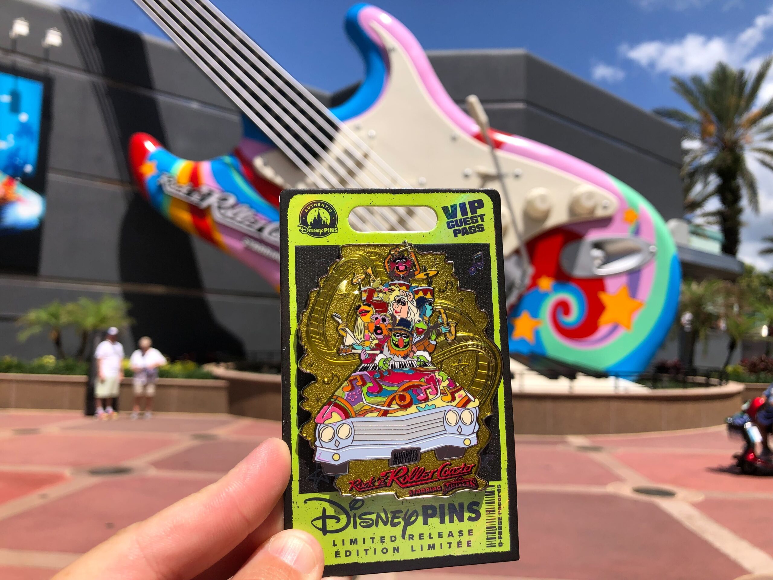 The pin features the crew on the psychedelic ride vehicle in front of the gold-tone track.