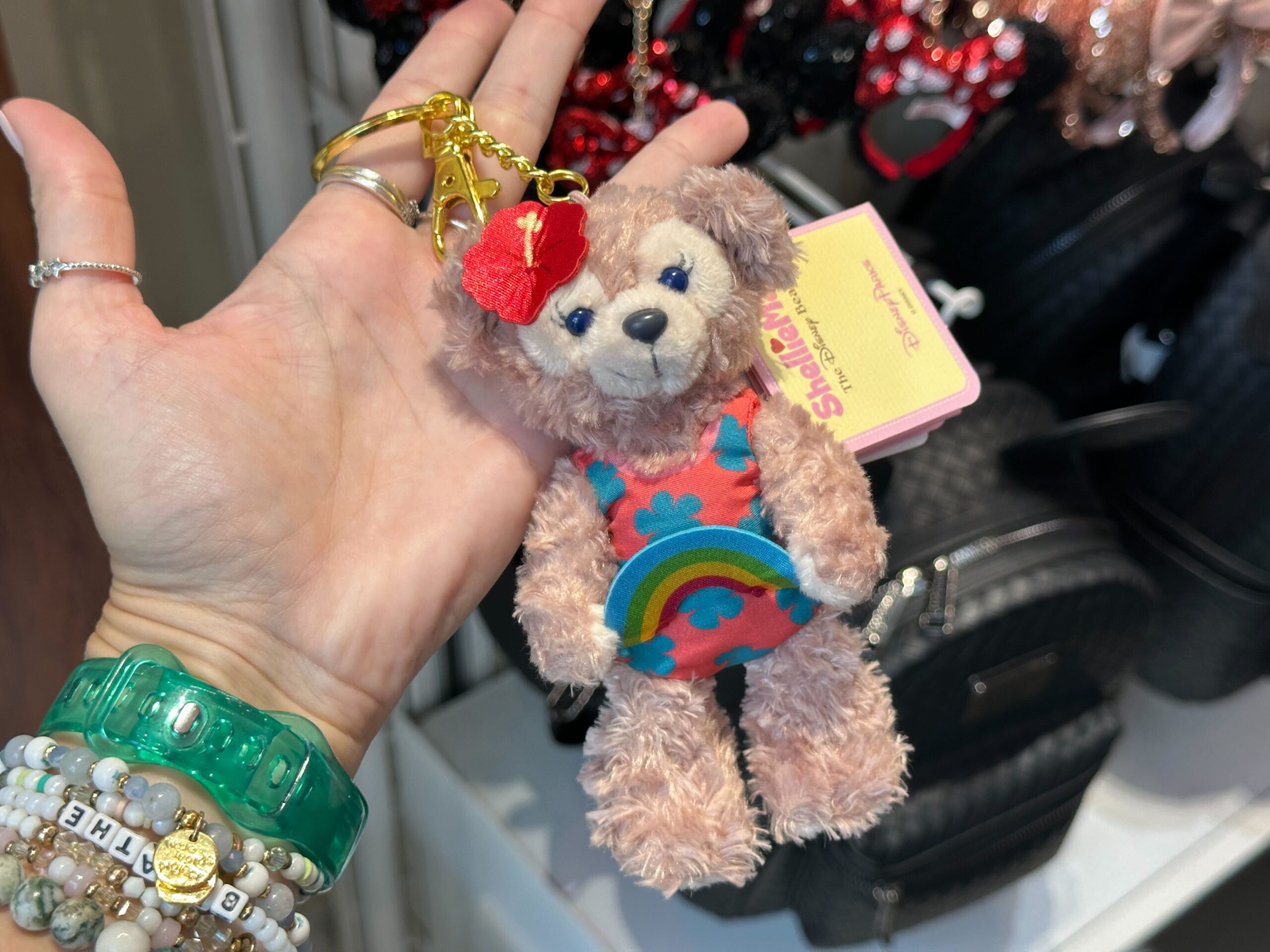 ShellieMay wears a one-piece swimsuit in the same pattern as Duffy. She holds a felt rainbow in her hands and has a red tropical flower on her head.