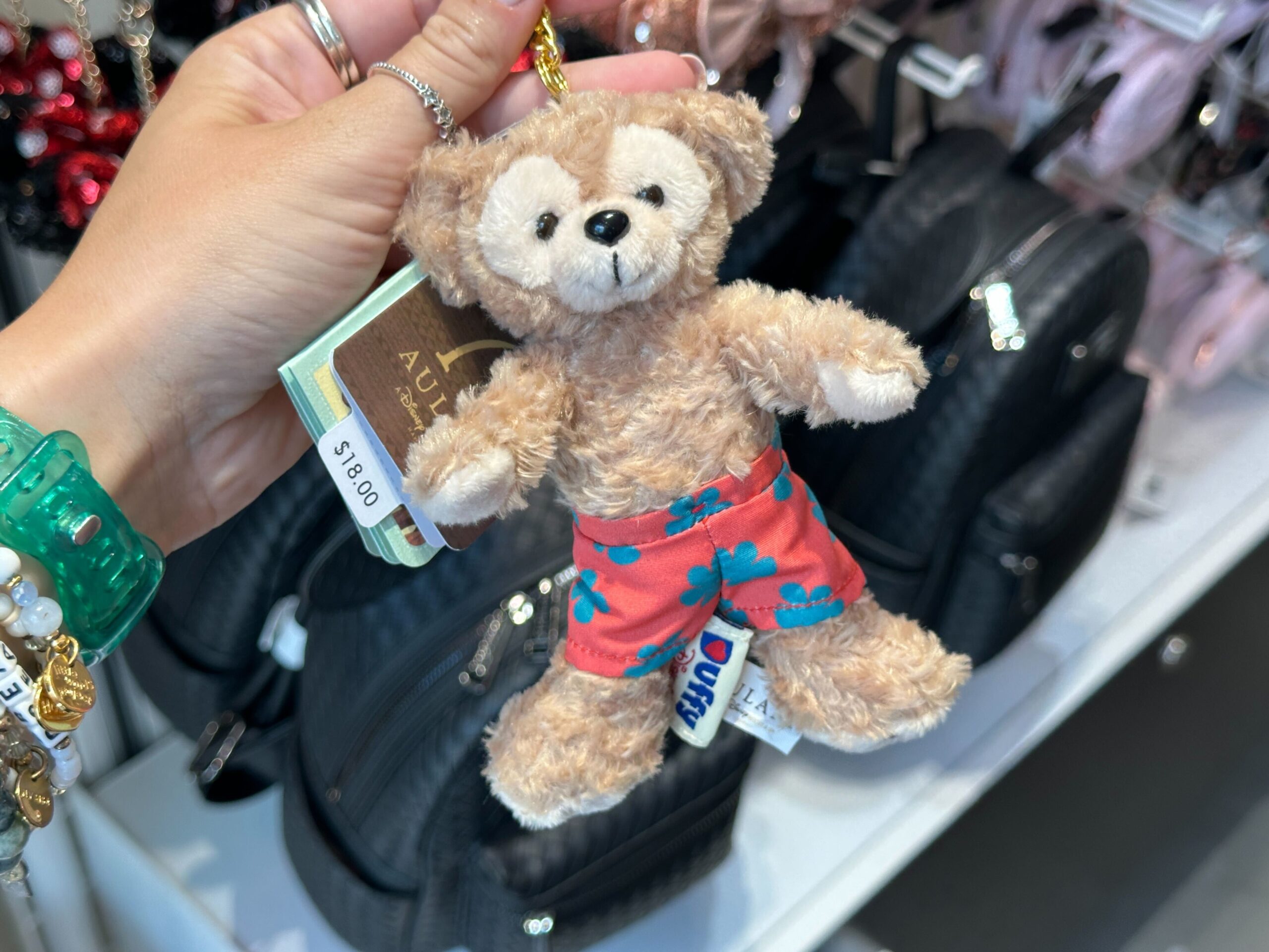 This keychain has gold-tone hardware attached to a mini plush of Duffy. He wears coral and blue floral-patterned swim shorts with an embroidered Mickey icon on the back.