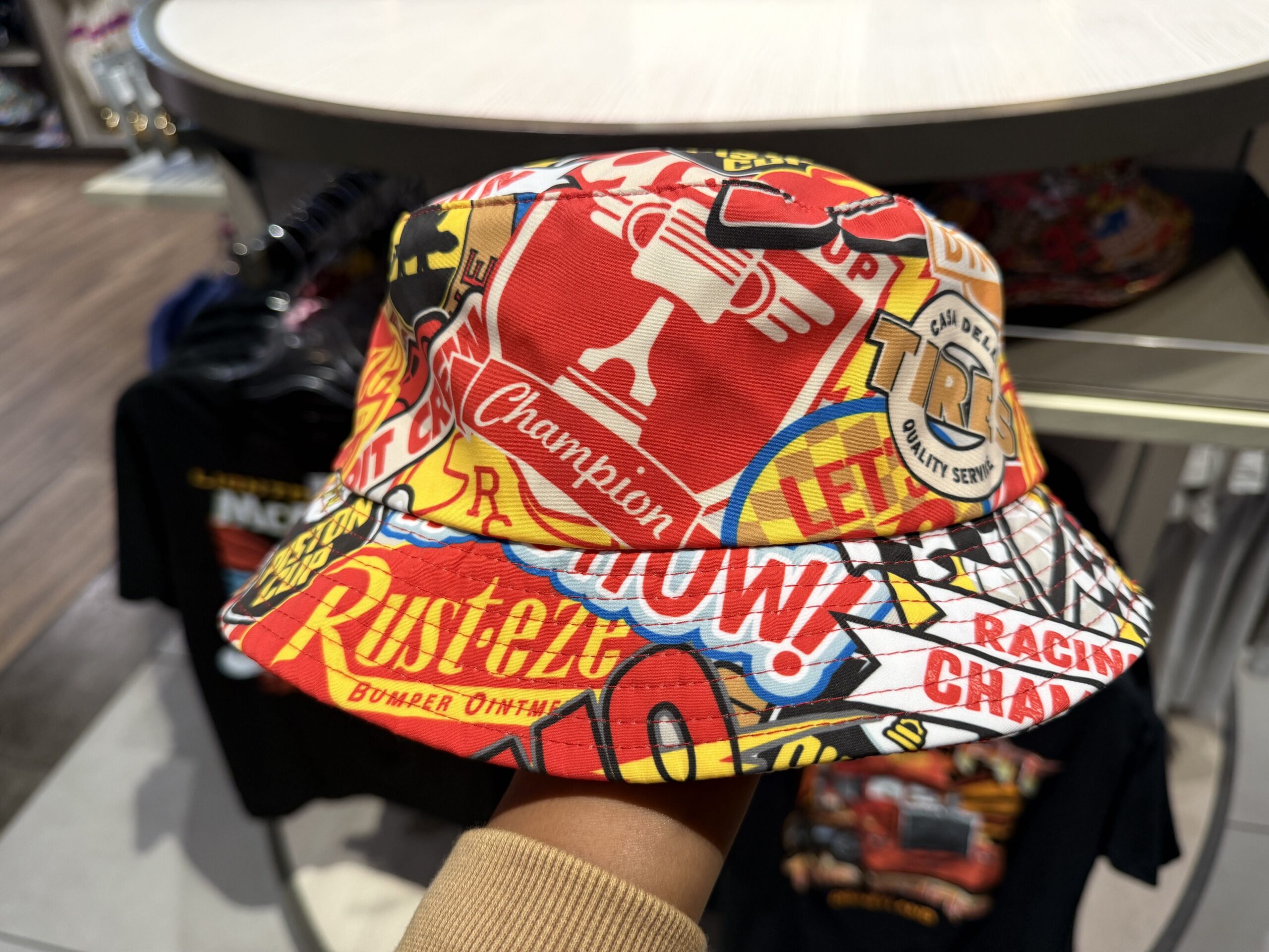 This bucket hat is absolutely covered in Piston Cup and racing iconography seen in the Cars film. From the Piston Cup champion imagery to a Rust-eze ad, Dinoco Gasoline logo, and more.