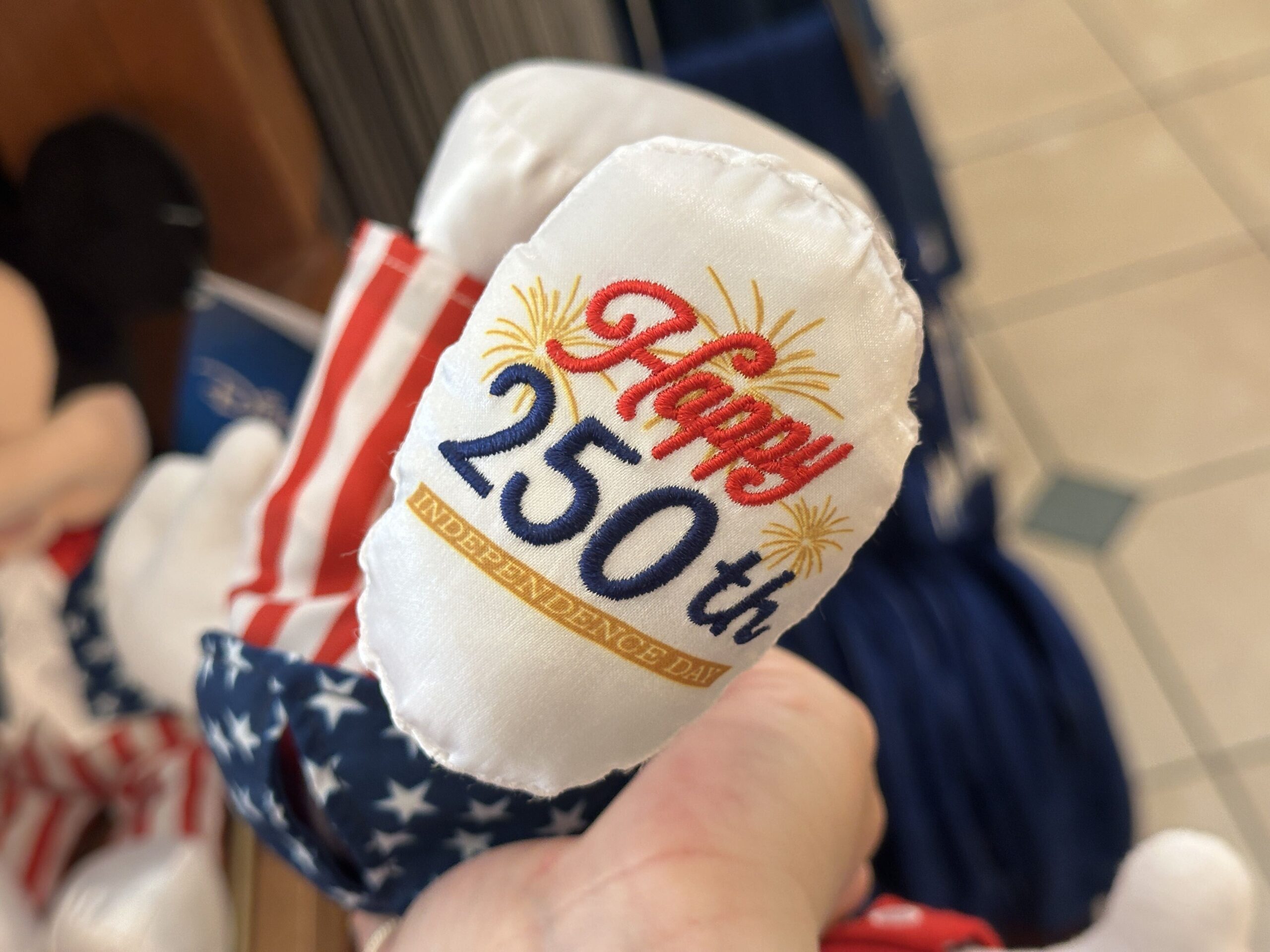 The plush’s oversized white shoes feature a special embroidered design celebrating the occasion. One of Mickey's shoes includes the phrase “Happy 250th" with "Independence Day" underneath in white lettering lying on a gold banner. Gold embroidered fireworks burst around the text, adding a festive touch to the commemorative plush.