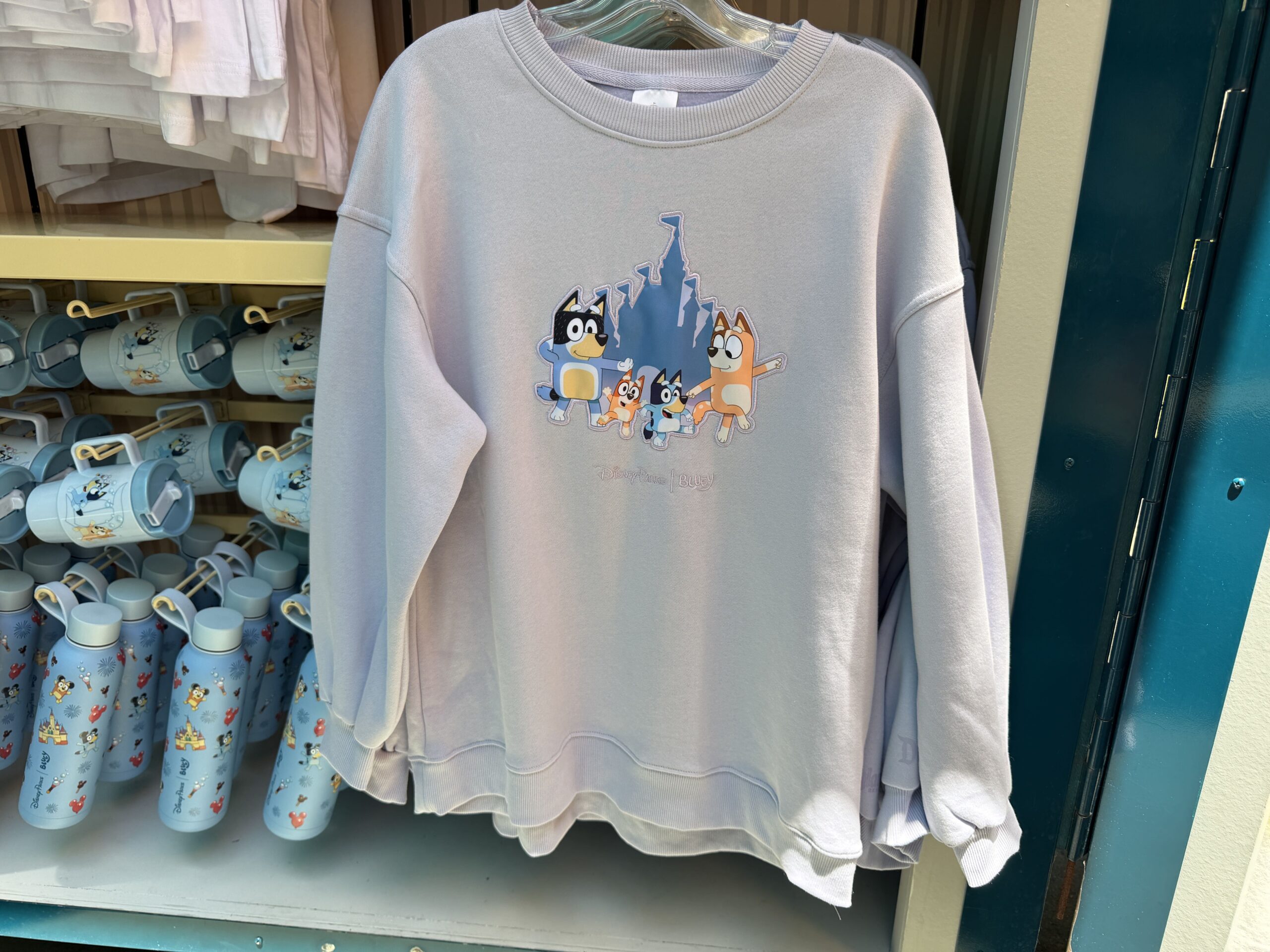 In lavender, this pullover shows the whole Heeler Family dancing in front of a Fantasyland Castle. Beneath them is the Disney Parks | Bluey wordmark.