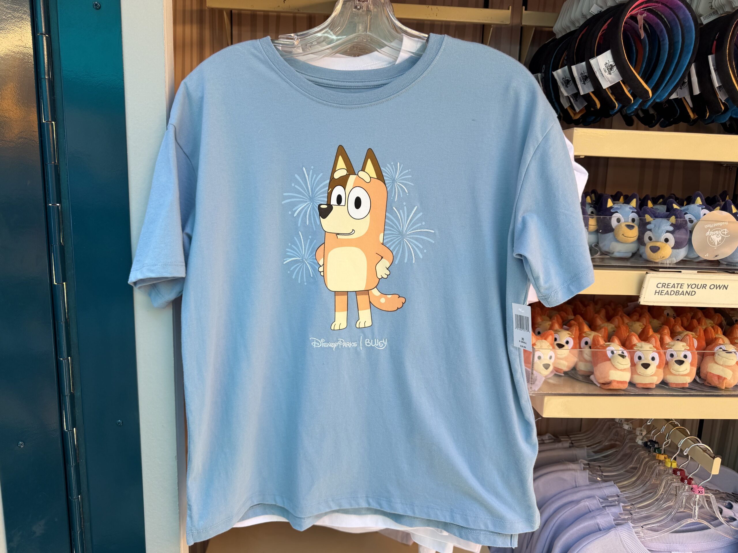 Chili is standing with her hands on her hips with embroidered fireworks on either side of her. This t-shirt is light blue with the fireworks in a matching color. Beneath Chili is the Disney Parks | Bluey wordmark. One of the sleeves says "Disneyland" in light blue.