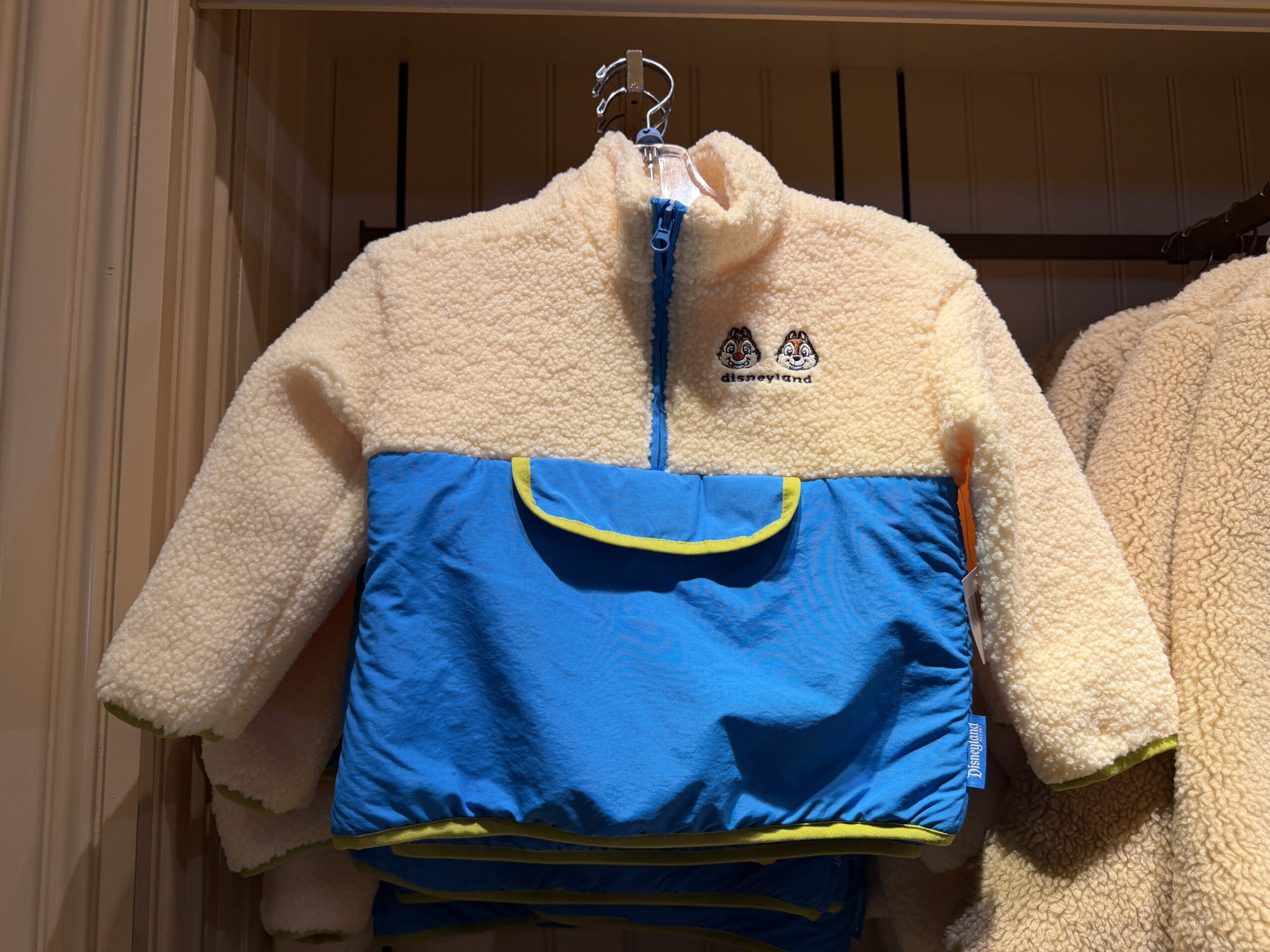 In a similar style, but slightly lighter, this half-zip fleece jacket has a lighter tan sherpa fleece. Chip 'n' Dale are shown on the left chest above an embroidered "Disneyland." The bottom half of the jacket is more like a blue rain jacket material than a fleece.