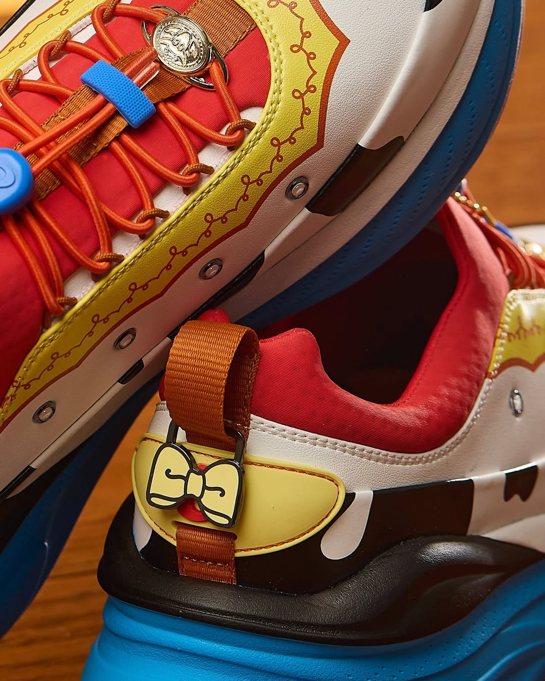 The Jessie shoes are red on top, followed by yellow printed trim based on her collar. Jessie's belt buckle is on the laces, and a bow appliqué is on the back. There is a cow print stripe around the side and blue across the bottom.