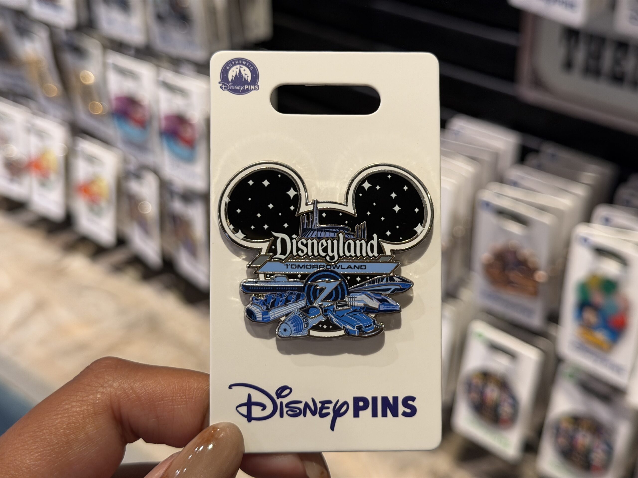 The new open edition Tomorrowland pin depicts Space Mountain and various Tomorrowland ride vehicles in shades of blue: a Space Mountain rocket, an Astro Orbitors rocket, an Autopia car, a Star Tours StarSpeeder, and a Monorail. In the center is a Buzz Lightyear Astro Blasters "Z" target.