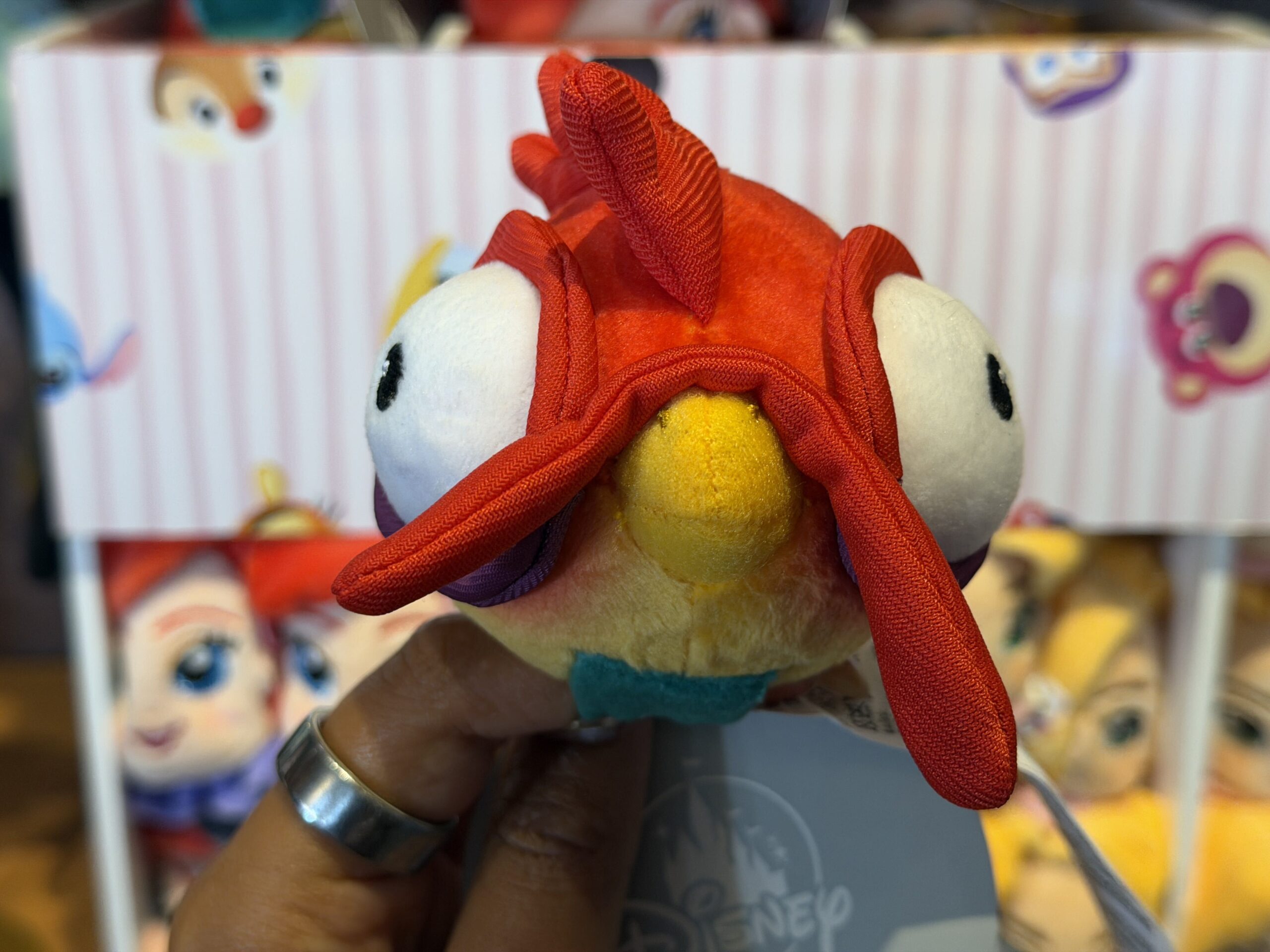 Heihei's bright red wattle and comb stick out from the design of this plush accessory. His black, beady eyes are embroidered on either side of his head, giving him a goofy, almost cock-eyed appearance.