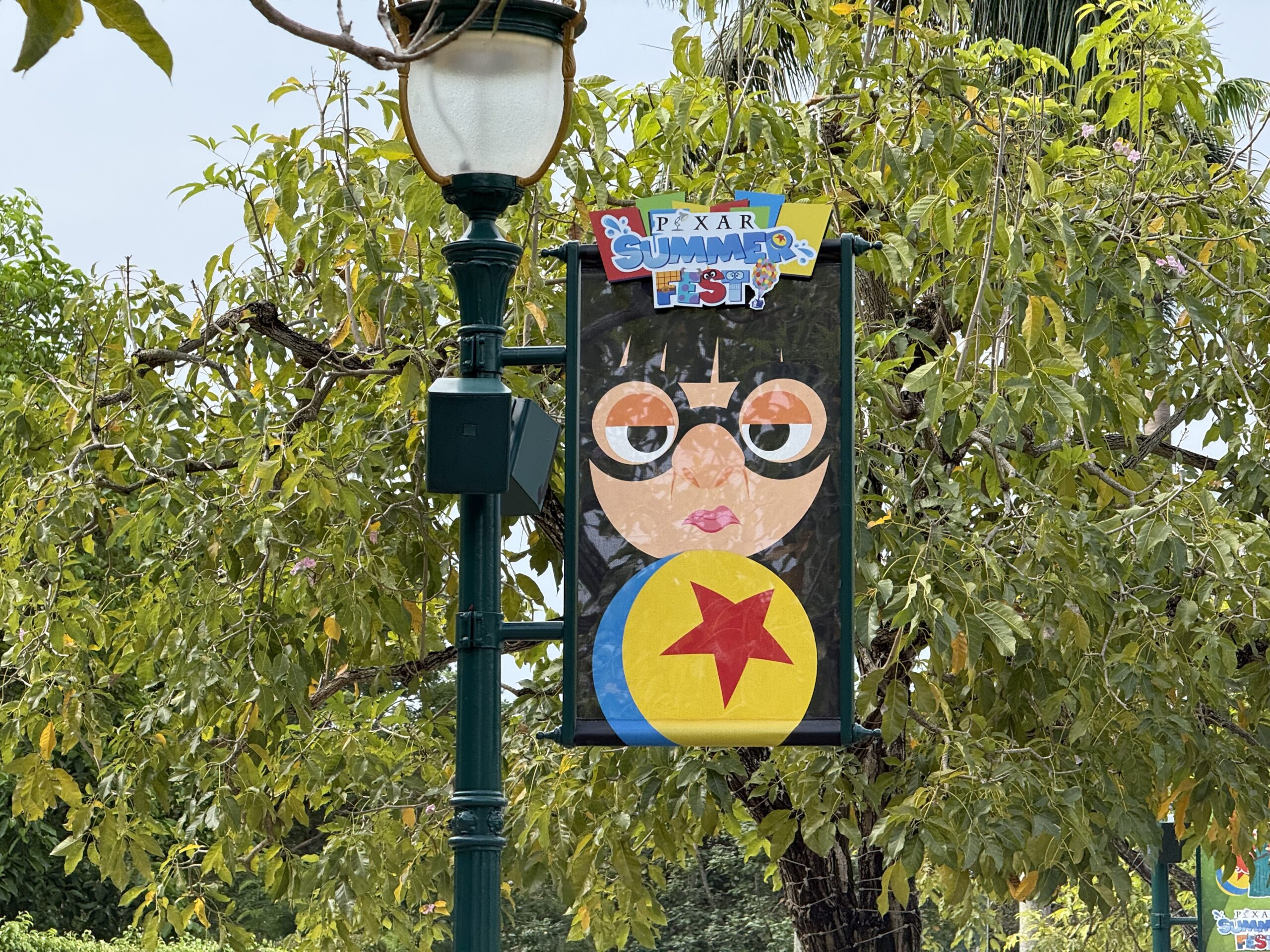 The walkway to the park entrance is lined with banners featuring Pixar characters and the Pixar Summer Fest logo.