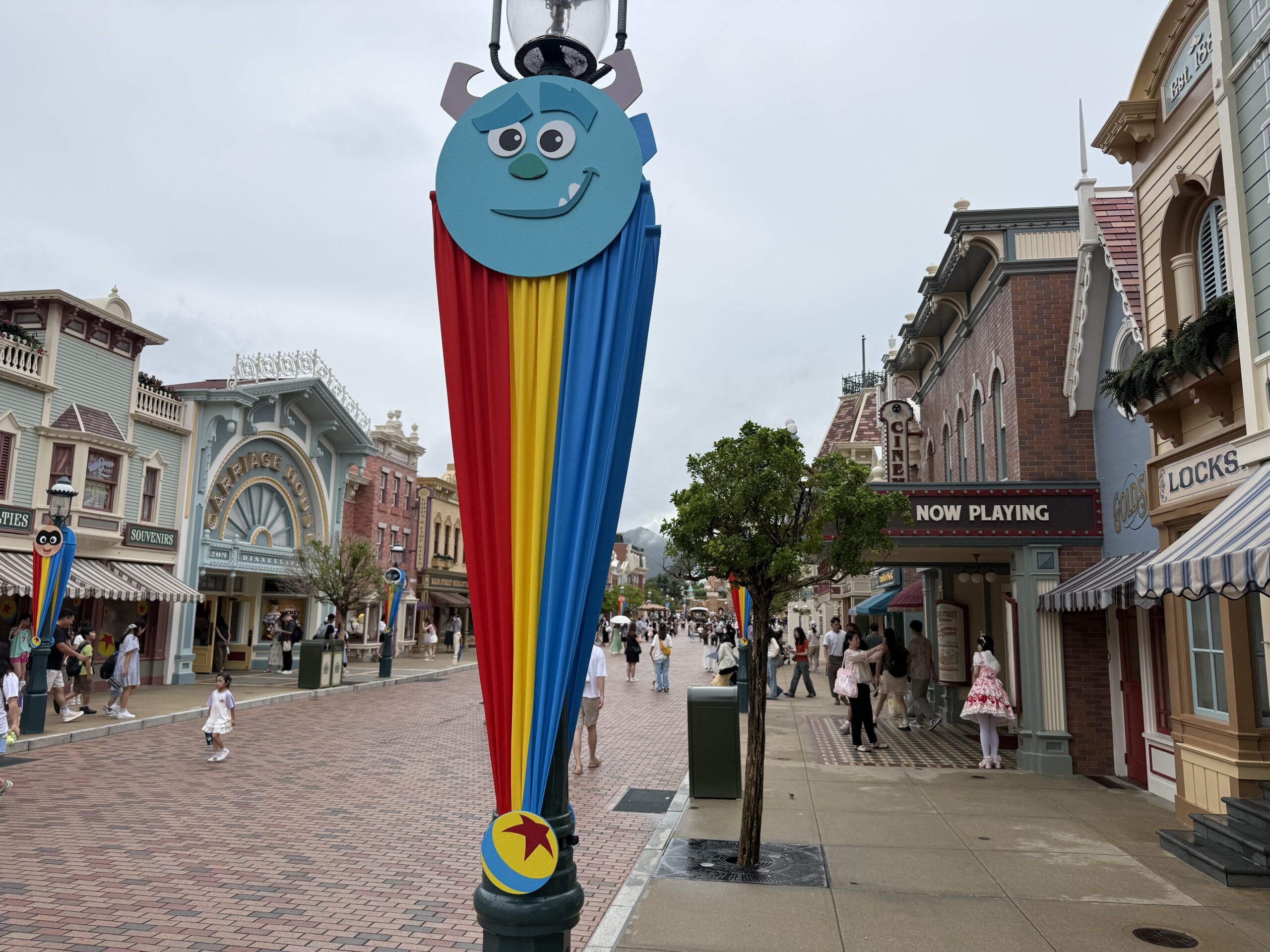 The Main Street lampposts are decorated with red, yellow, and blue striped banners. They are secured at the top with round character faces and at the bottom with a small Pixar ball element.