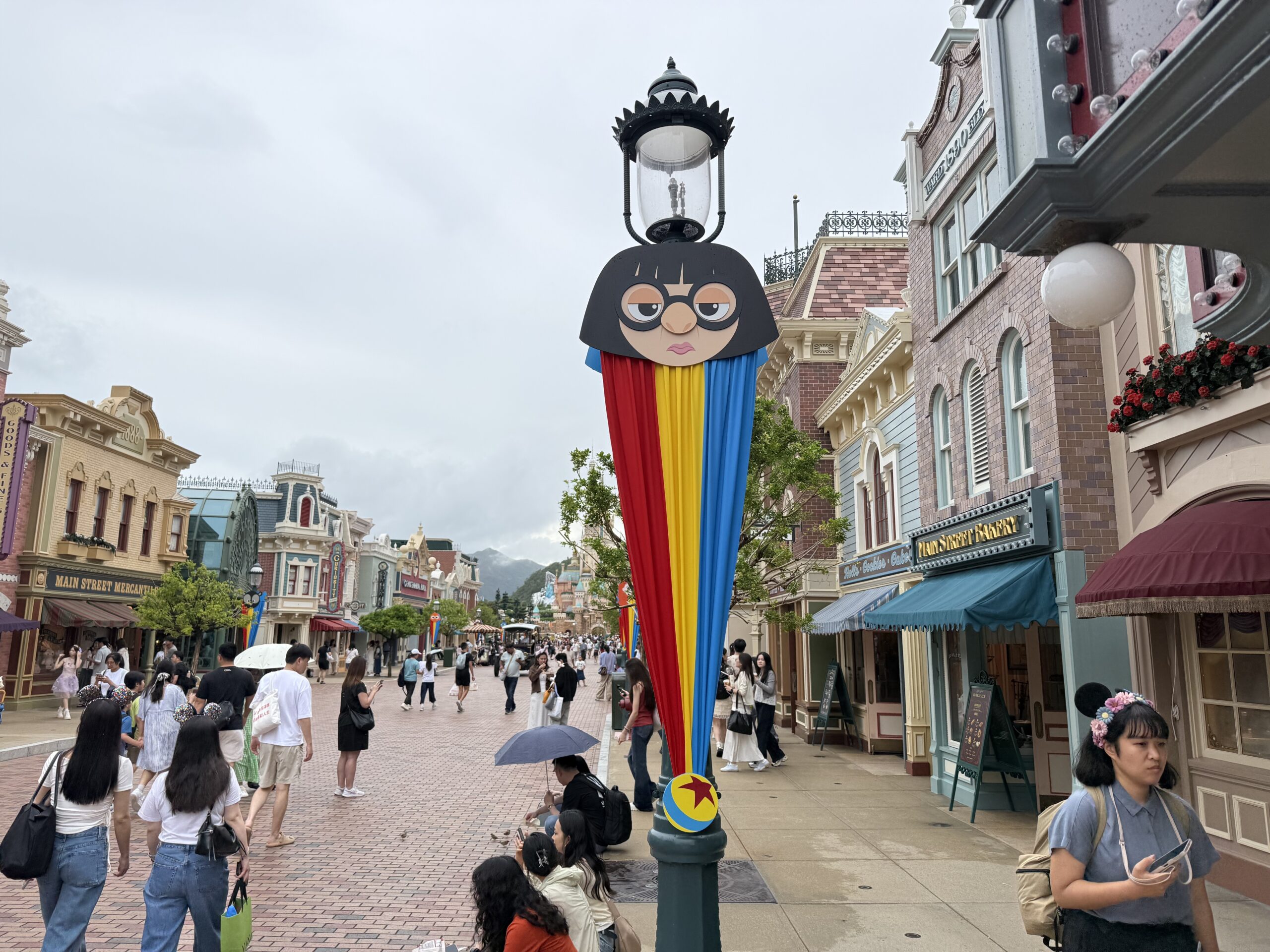 The Main Street lampposts are decorated with red, yellow, and blue striped banners. They are secured at the top with round character faces and at the bottom with a small Pixar ball element.