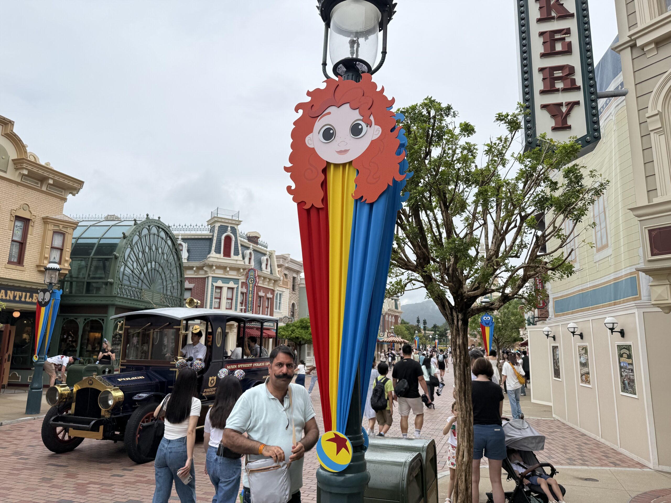 The Main Street lampposts are decorated with red, yellow, and blue striped banners. They are secured at the top with round character faces and at the bottom with a small Pixar ball element.