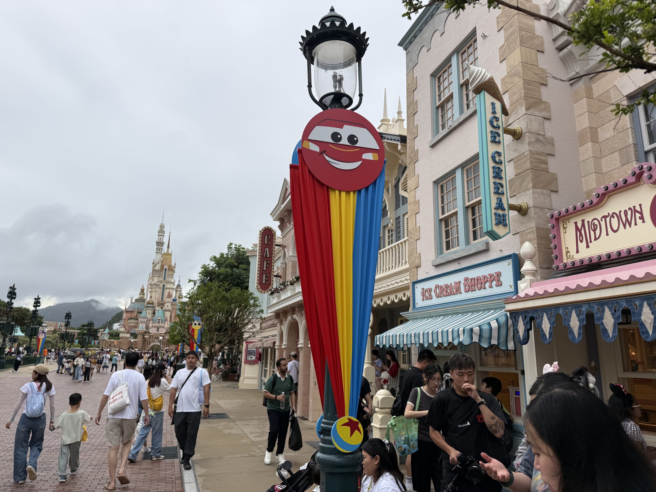 The Main Street lampposts are decorated with red, yellow, and blue striped banners. They are secured at the top with round character faces and at the bottom with a small Pixar ball element.
