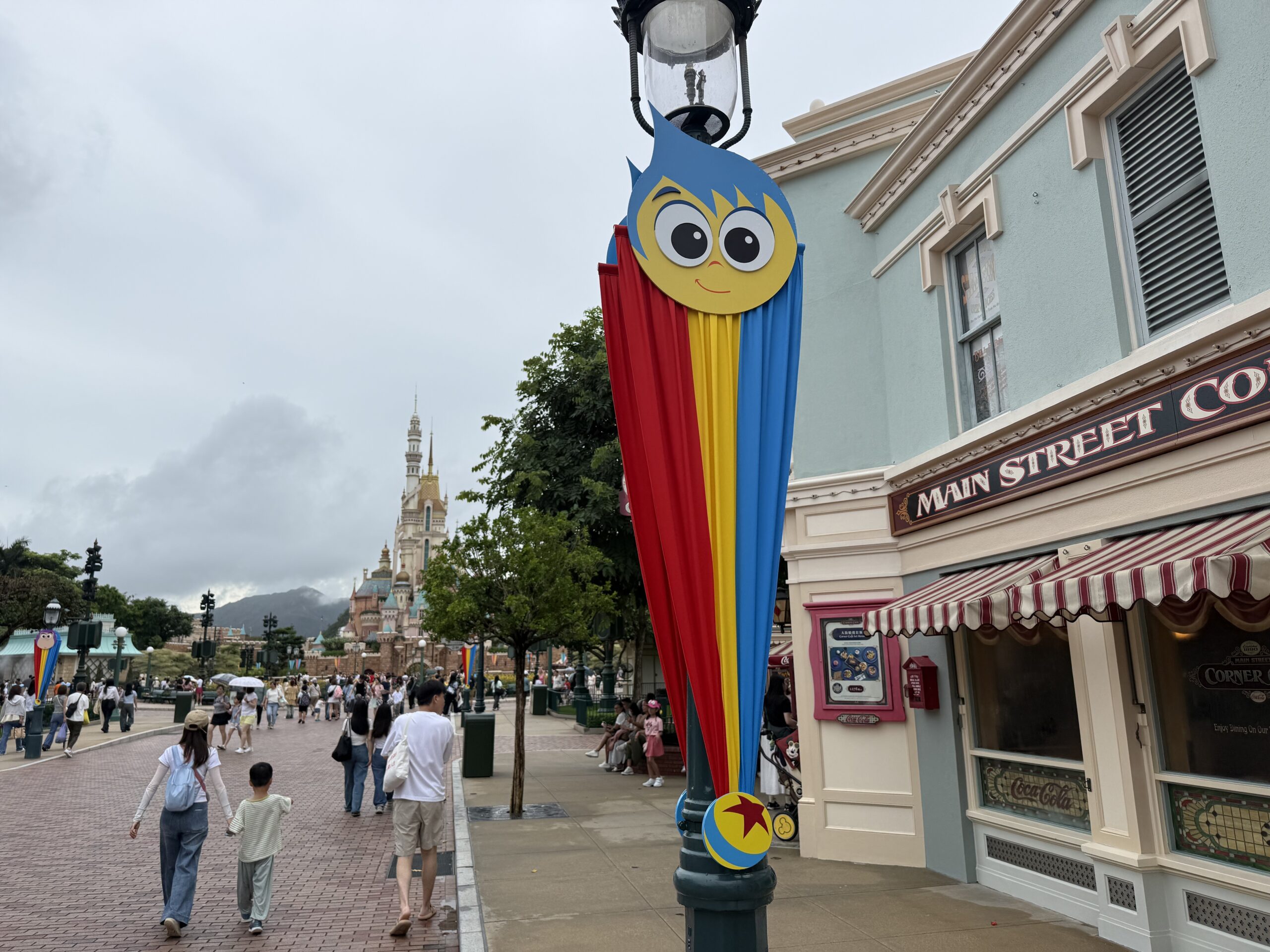The Main Street lampposts are decorated with red, yellow, and blue striped banners. They are secured at the top with round character faces and at the bottom with a small Pixar ball element.
