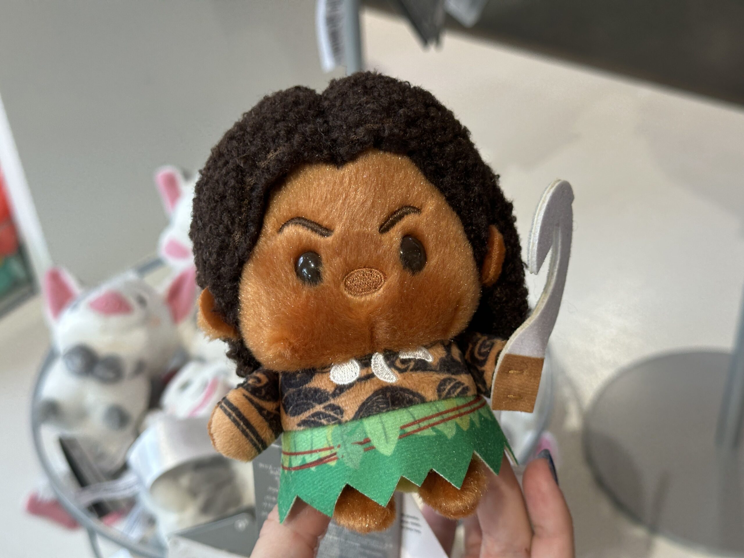 Maui's Urupocha-Chan plush is shown holding a felted version of his Fish Hook. His nose, necklace, and eyebrows are embroidered, and his grass skirt is felted.