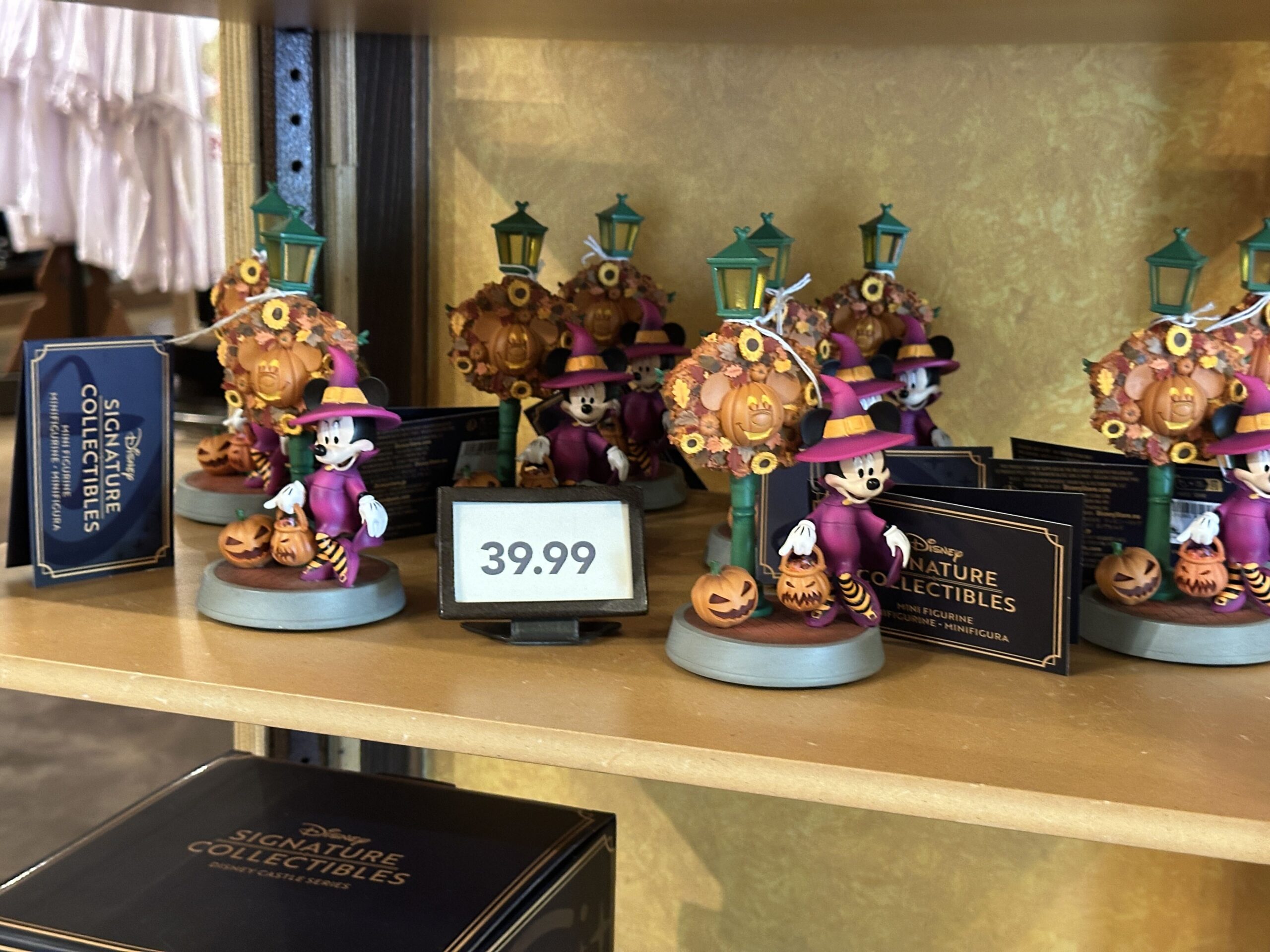 Part of the Disney Signature Collectibles collection, this figurine shows Minnie in her witch costume out trick-or-treating. She is standing beside a Main Street U.S.A. lightpole decorated with an autumnal wreath and a Mickey-shaped Jack-o-Lantern.