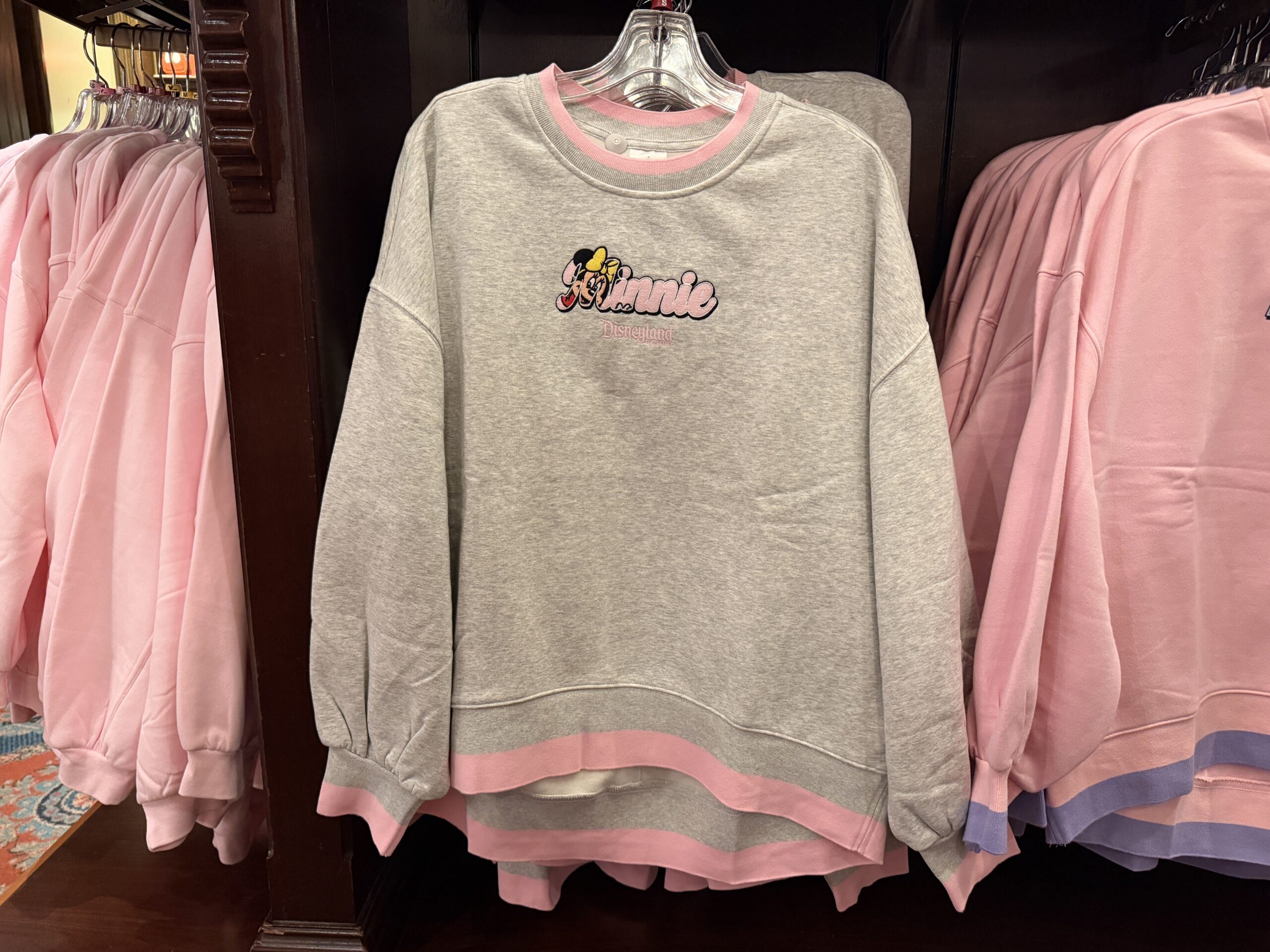 This heather gray pullover has a pink band along the neck, waist, and sleeve hems. Minnie, in a retro look, is shown in her name "Minnie" across the chest. Beneath is the Disneyland Resort wordmark in a matching pink.