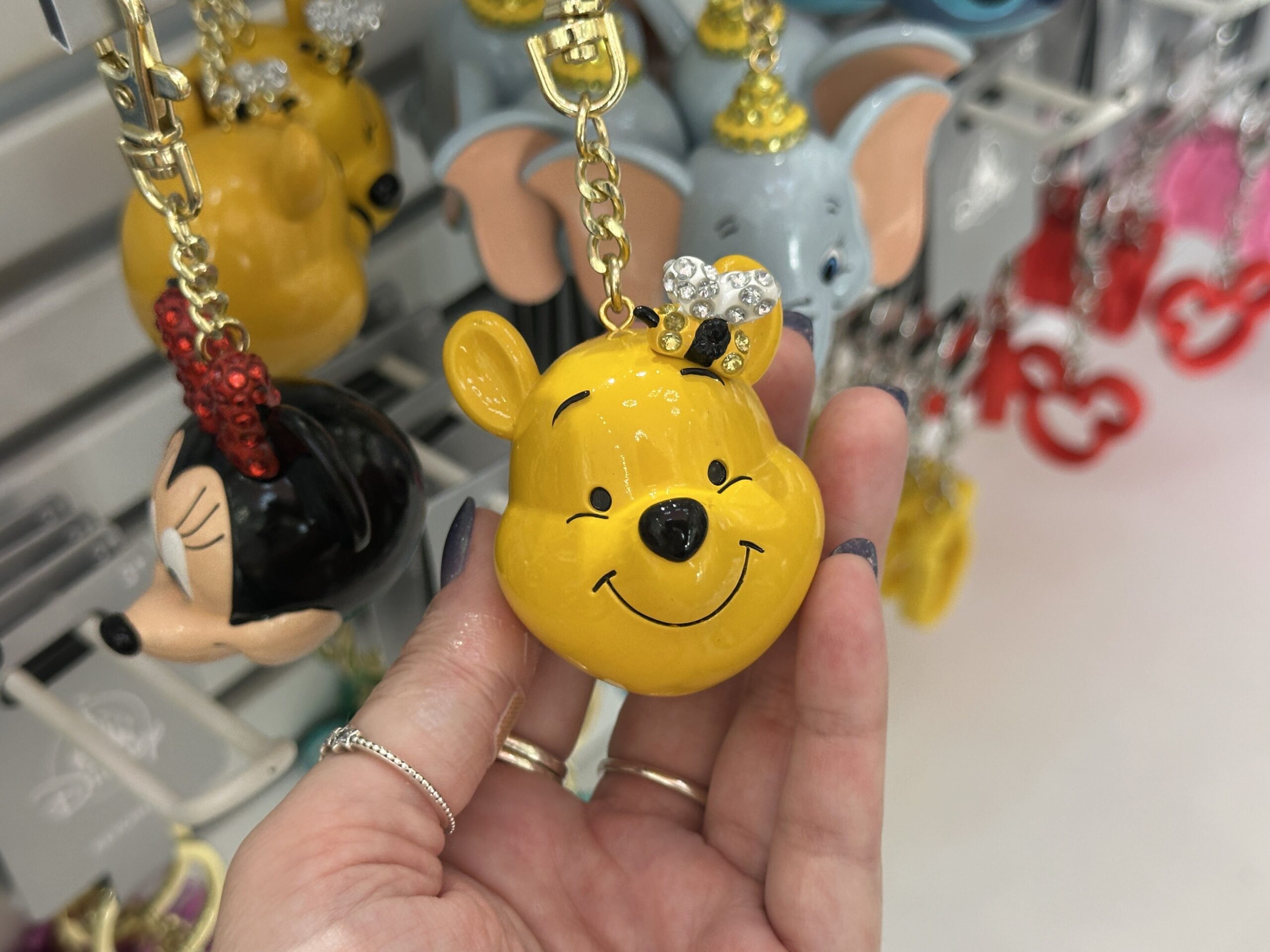 This keychain is sculpted to look like Winnie the Pooh. His smiling yellow face is adorned with a gem-studded bee by one of his ears.
