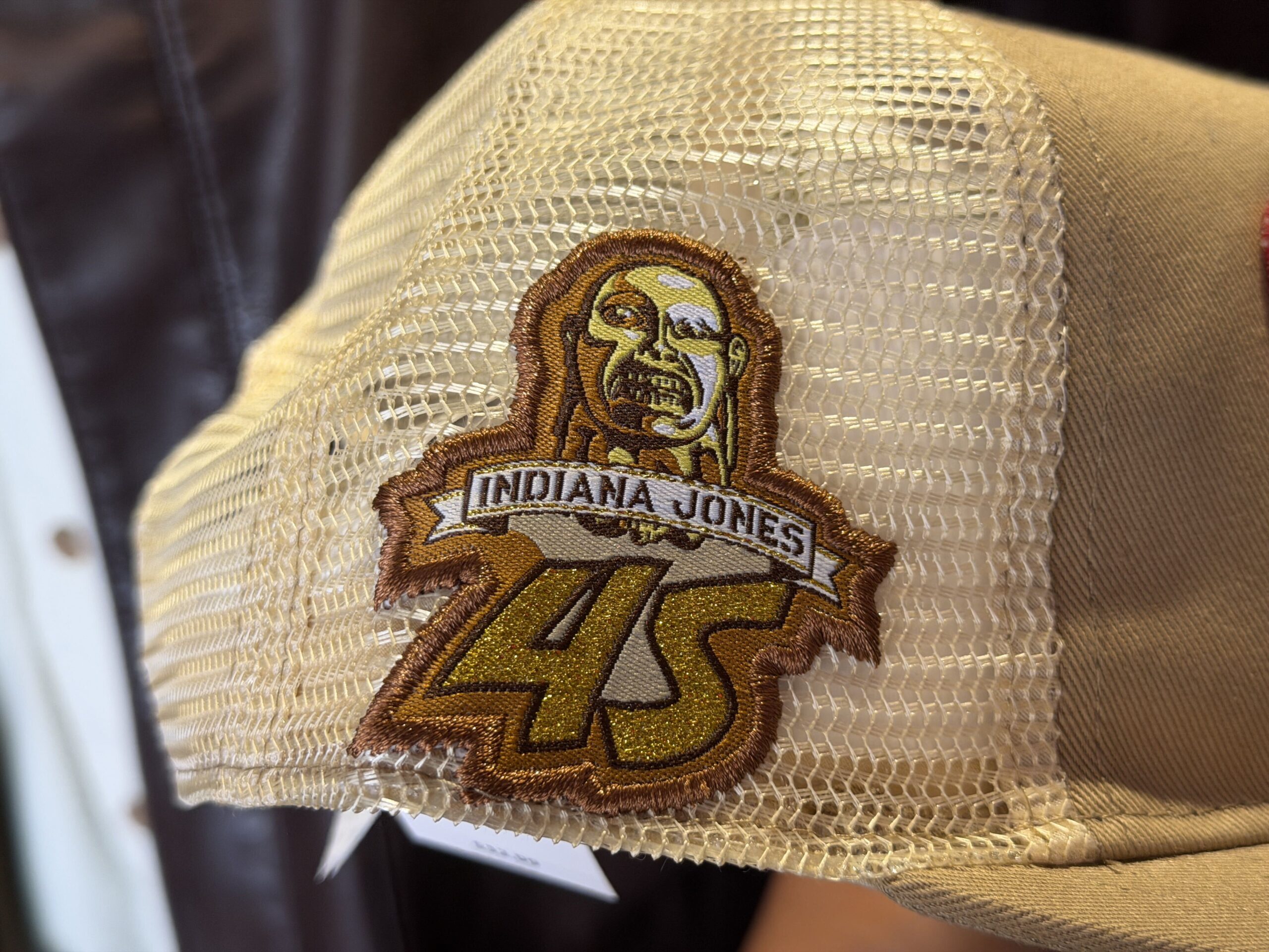 On the righthand side of the hat is a patch that reads "Indiana Jones" and "45." The Chachapoyan Fertility Idol (or Golden Idol) that Indy takes is shown at the top of the patch.