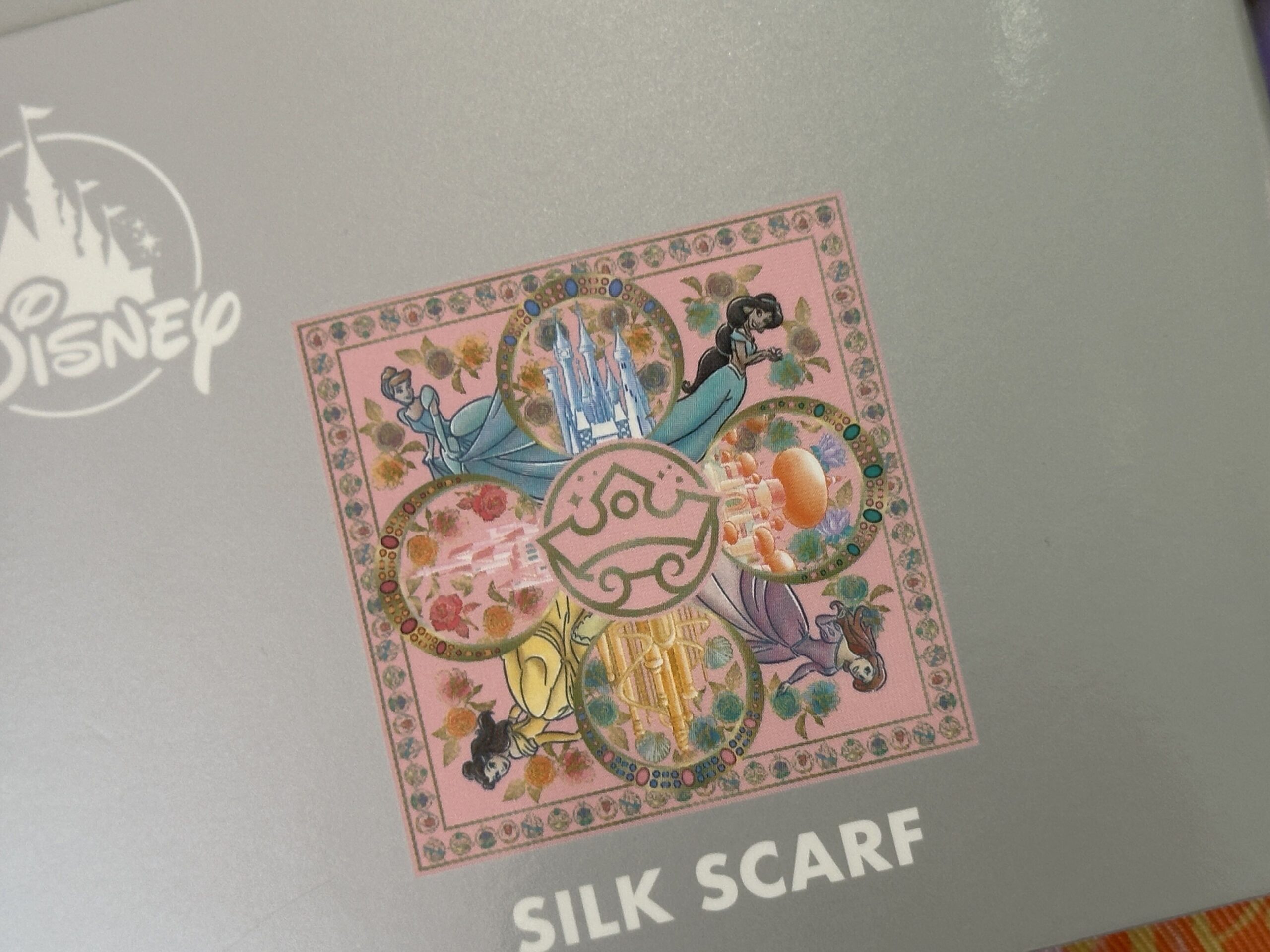 The silk scarf is folded up and comes in gray packaging that shows the full design as well as potential ways to wear the scarf.