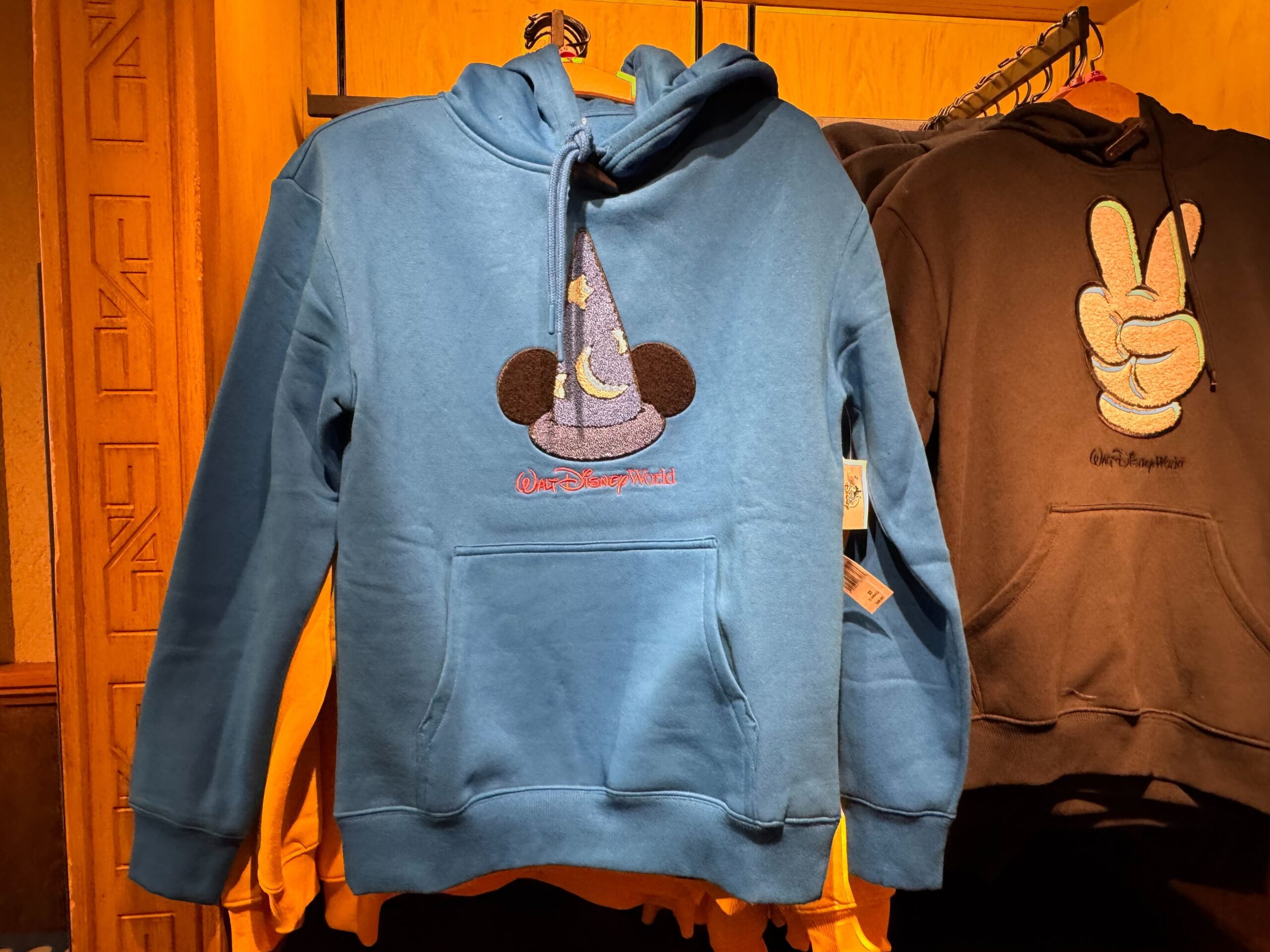 In a denim blue, this pullover hooded sweatshirt has a kangaroo pocket in the front and a fuzzy Sorcerer Mickey patch on the center chest. Beneath the hat is the Walt Disney World wordmark embroidered in red.