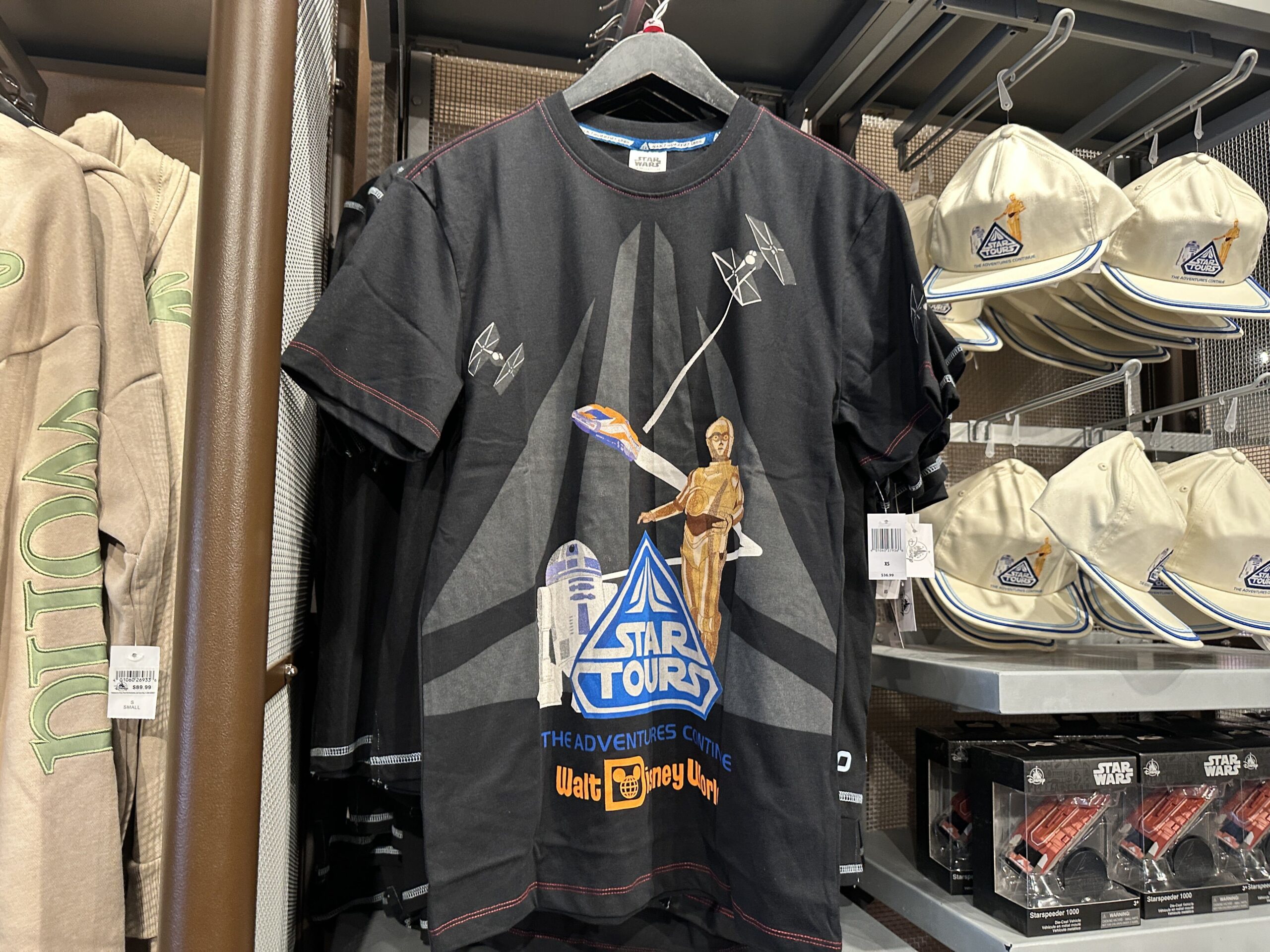 On the same ride topic, there is a new Star Tours t-shirt available as well. The Star Tours: The Adventures Continue logo is on the front above the Walt Disney World wordmark. This shirt is primarily black with an oversized gray Star Tours symbol in the background. TIE fighters are attacking the StarSpeeder in the background while C3-PO and R2-D2 are standing in the foreground.