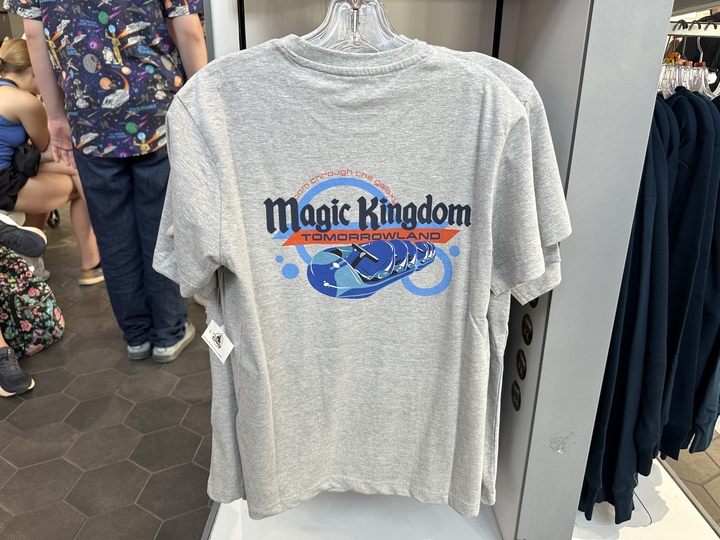 The heather gray T-shirt has the park's Magic Kingdom text logo and Tomorrowland above a Space Mountain ride vehicle on the back. The front has a small icon of the exterior of Space Mountain, the Magic Kingdom logo, and Tomorrowland text.