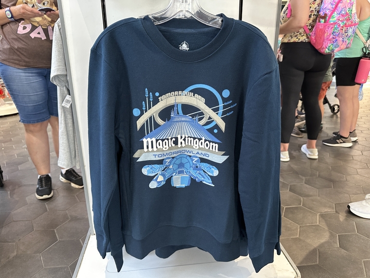 This dark blue sweatshirt has the park's Magic Kingdom text logo in white and Space Mountain prominently featured in the center. Ride vehicles on the lower half are made up of a pair from Space Mountain, Tomorrowland TTA PeopleMover, Tomorrowland Speedway, Astro Orbiter and a pair of targets from Buzz Lightyear’s Space Ranger Spin.