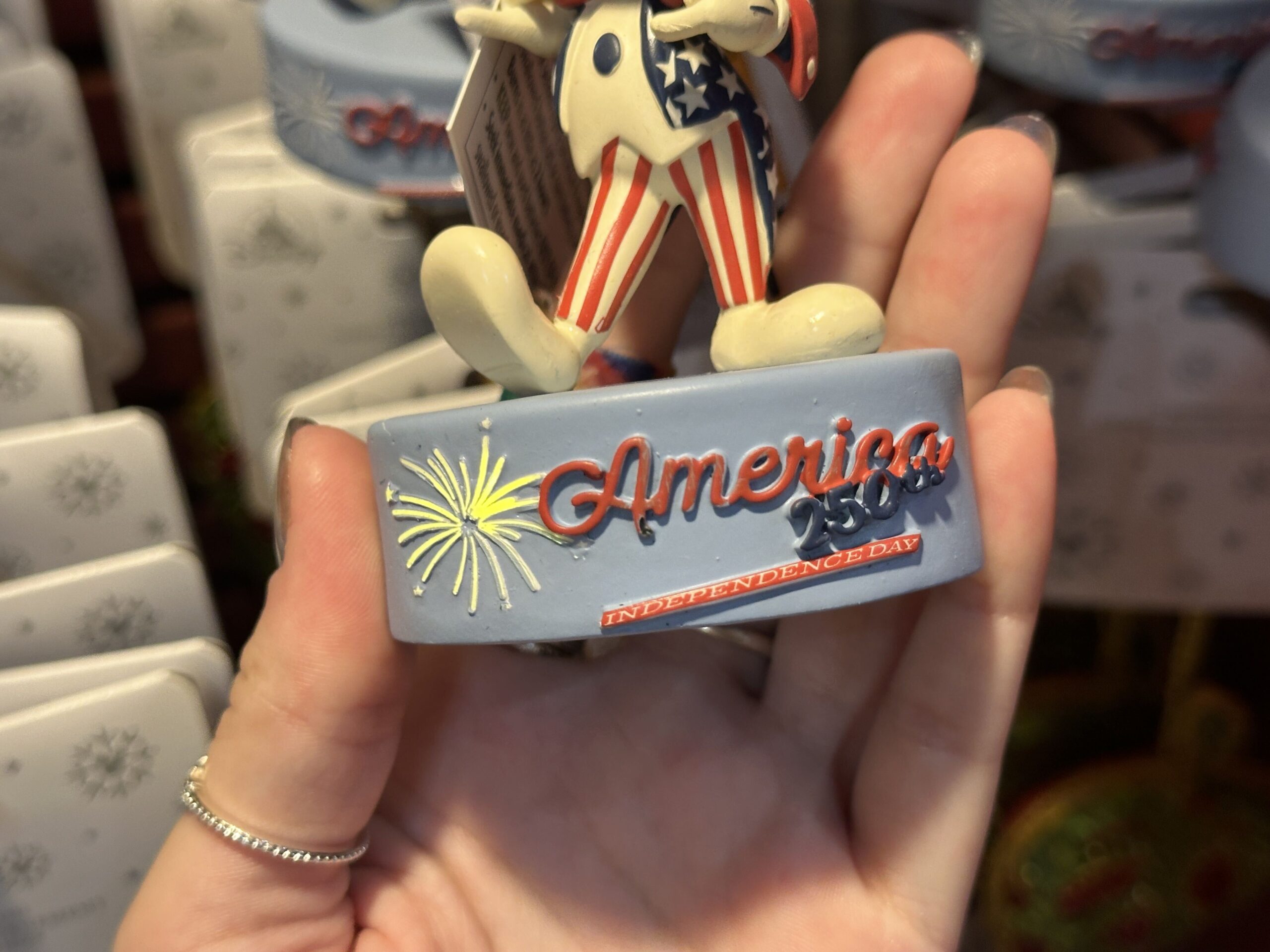Honoring 250 years of the United States, this ornament depicts Mickey in a red, white, and blue tuxedo. His pants are striped, and his jacket is covered in stars. Instead of black ears, they are dark blue.