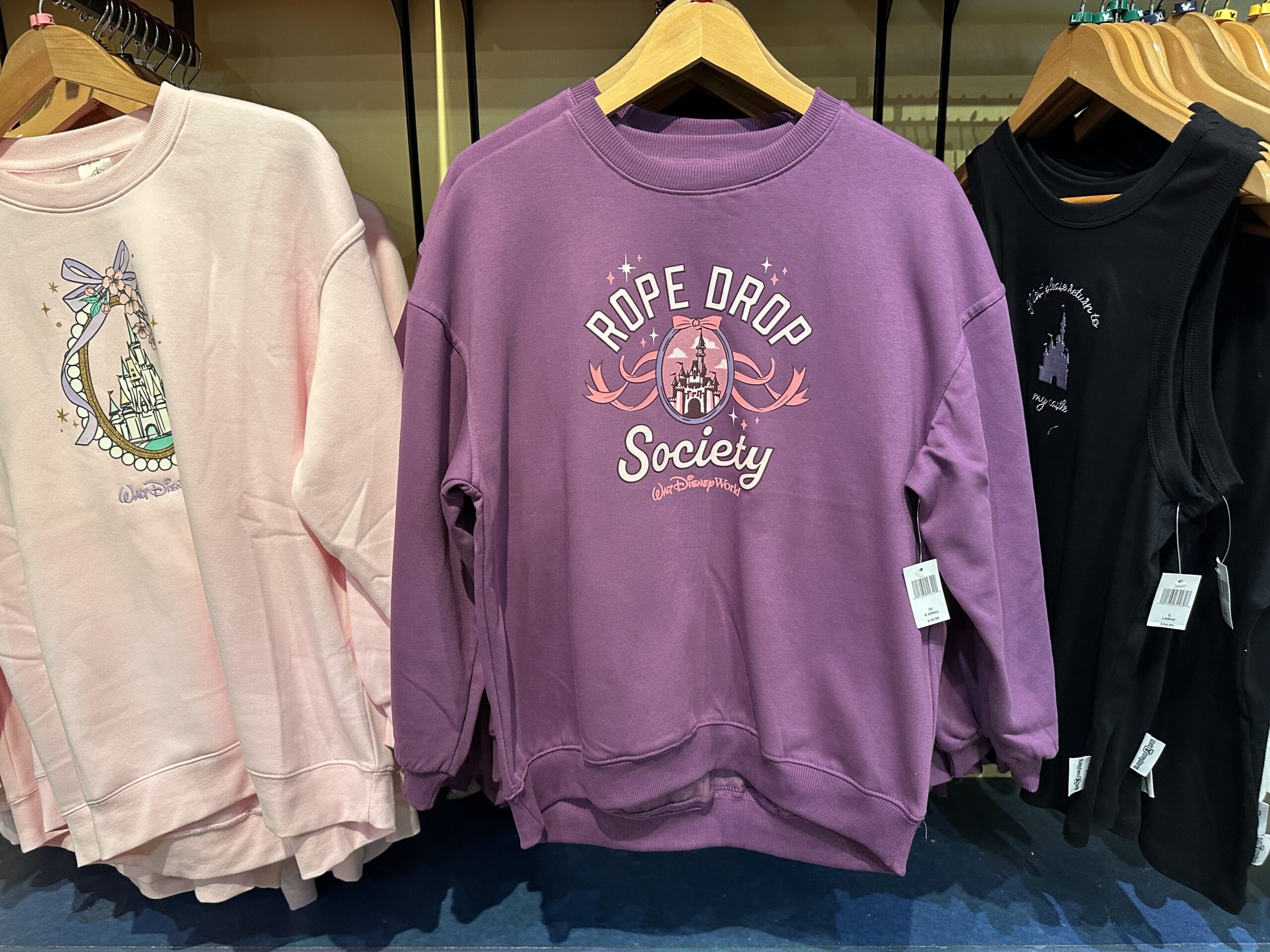 On the front of the sweater, "Rope Drop Society" is printed in a collegiate font around an image of Cinderella Castle. Bows and stars surround the design, and a pink Walt Disney World logo is printed beneath "Society."