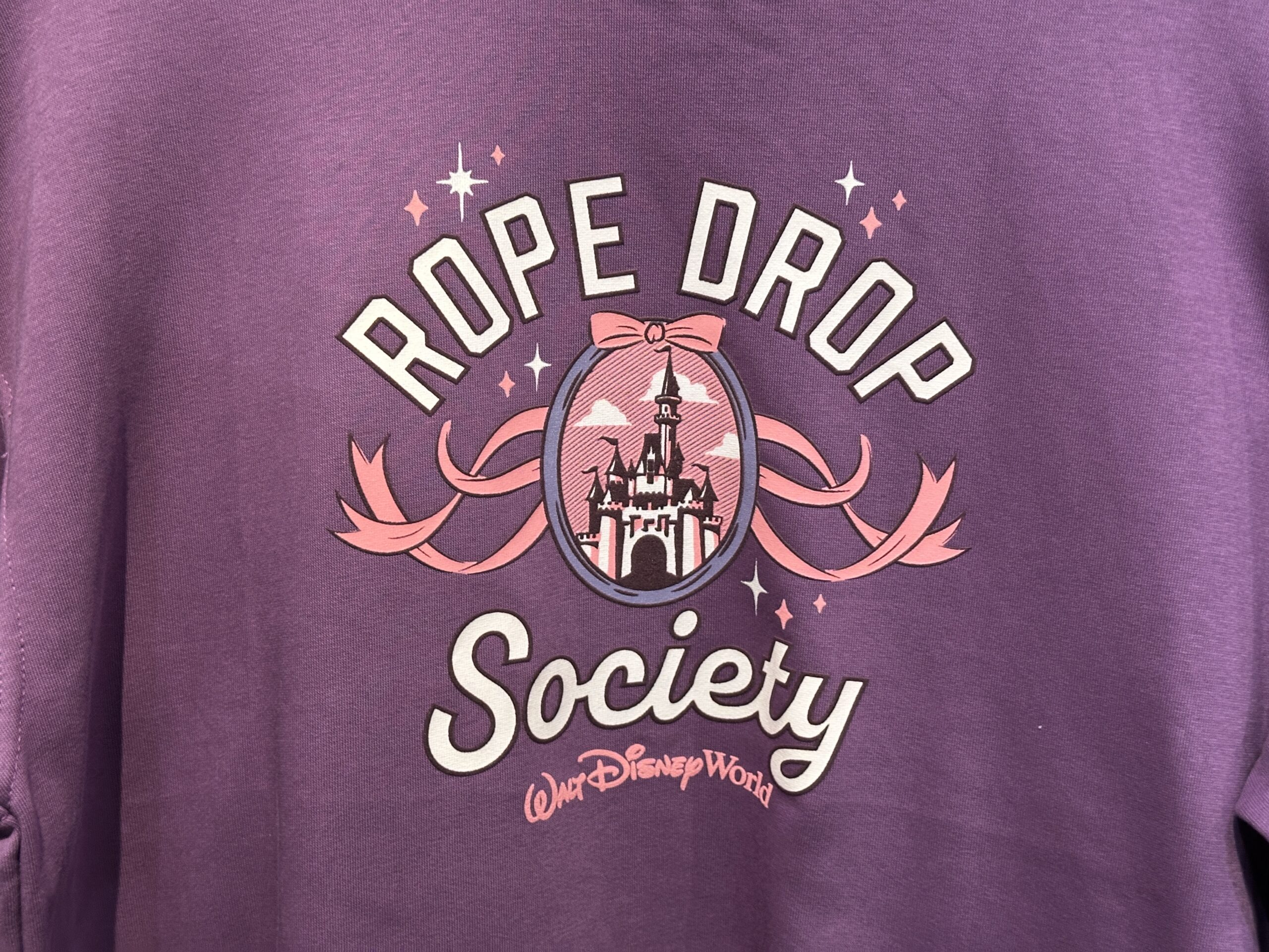 On the front of the sweater, "Rope Drop Society" is printed in a collegiate font around an image of Cinderella Castle. Bows and stars surround the design, and a pink Walt Disney World logo is printed beneath "Society."