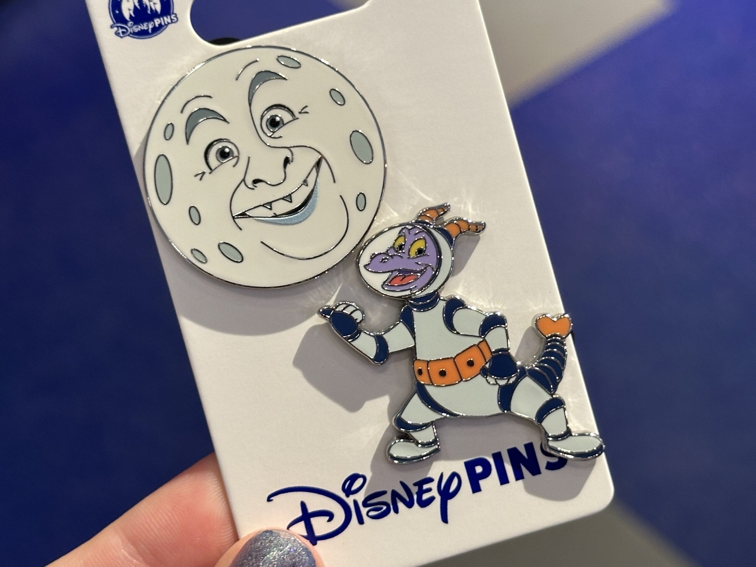 One pin depicts Dr. Nigel Channing's face on the moon as seen at the end of the ride's current iteration. The second pin is Figment in his spacesuit with a thumb out for hitchhiking. This version of Figment comes from the ride's original iteration.