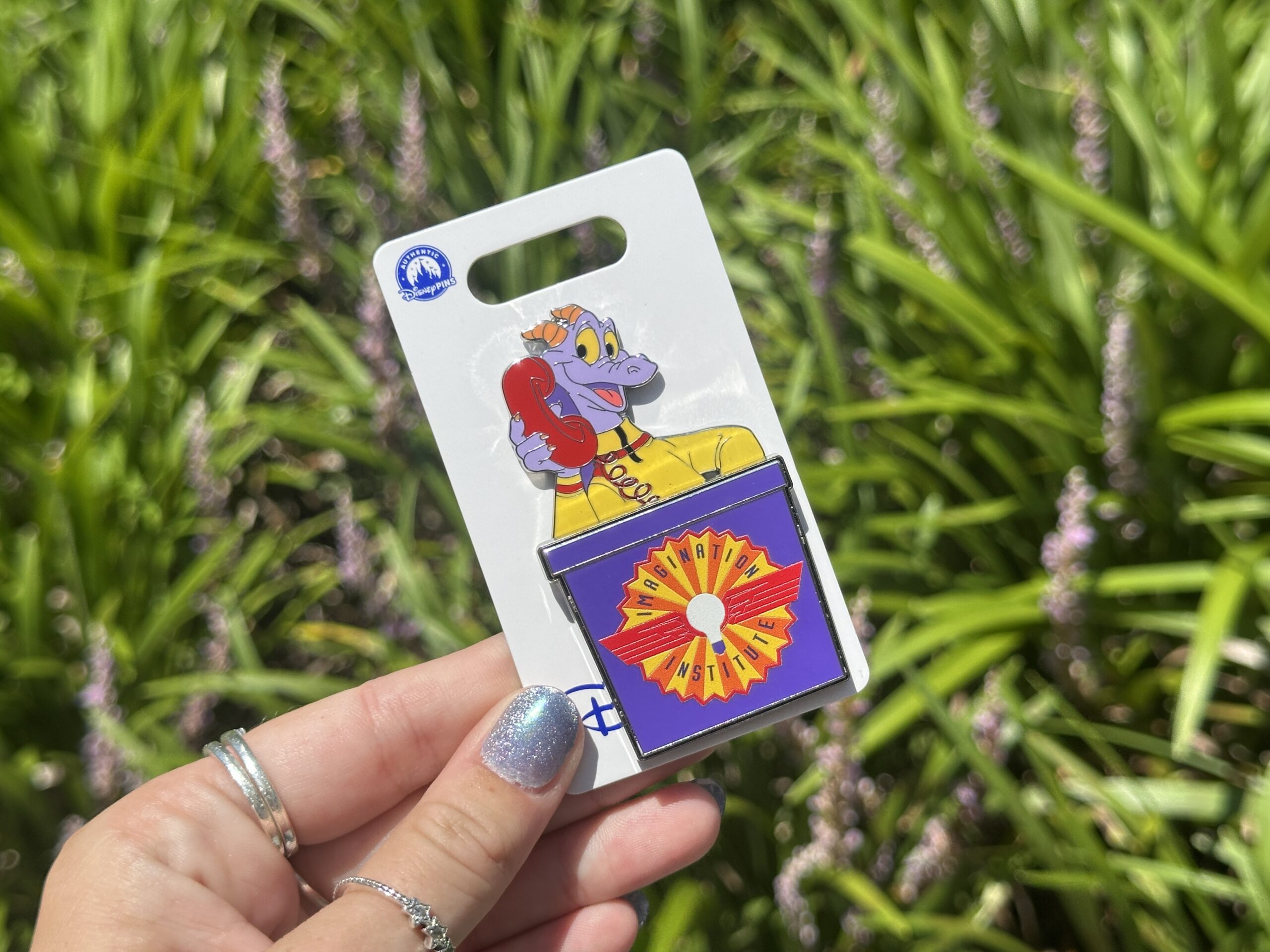 Inspired by the sound scene of Journey Into Imagination With Figment, this pin features Figment in his yellow sweater talking on a red phone. He pops out of a purple box featuring the Imagination Institute logo.