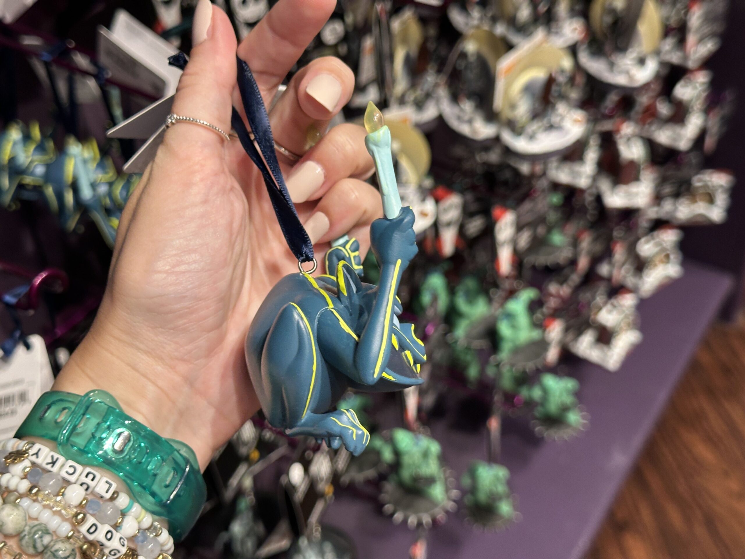 The gargoyle ornament similarly has yellow highlights against its blue-green exterior. It has a wide toothy mouth and sits in a crouched position. Two hands hold up a pair of candles.