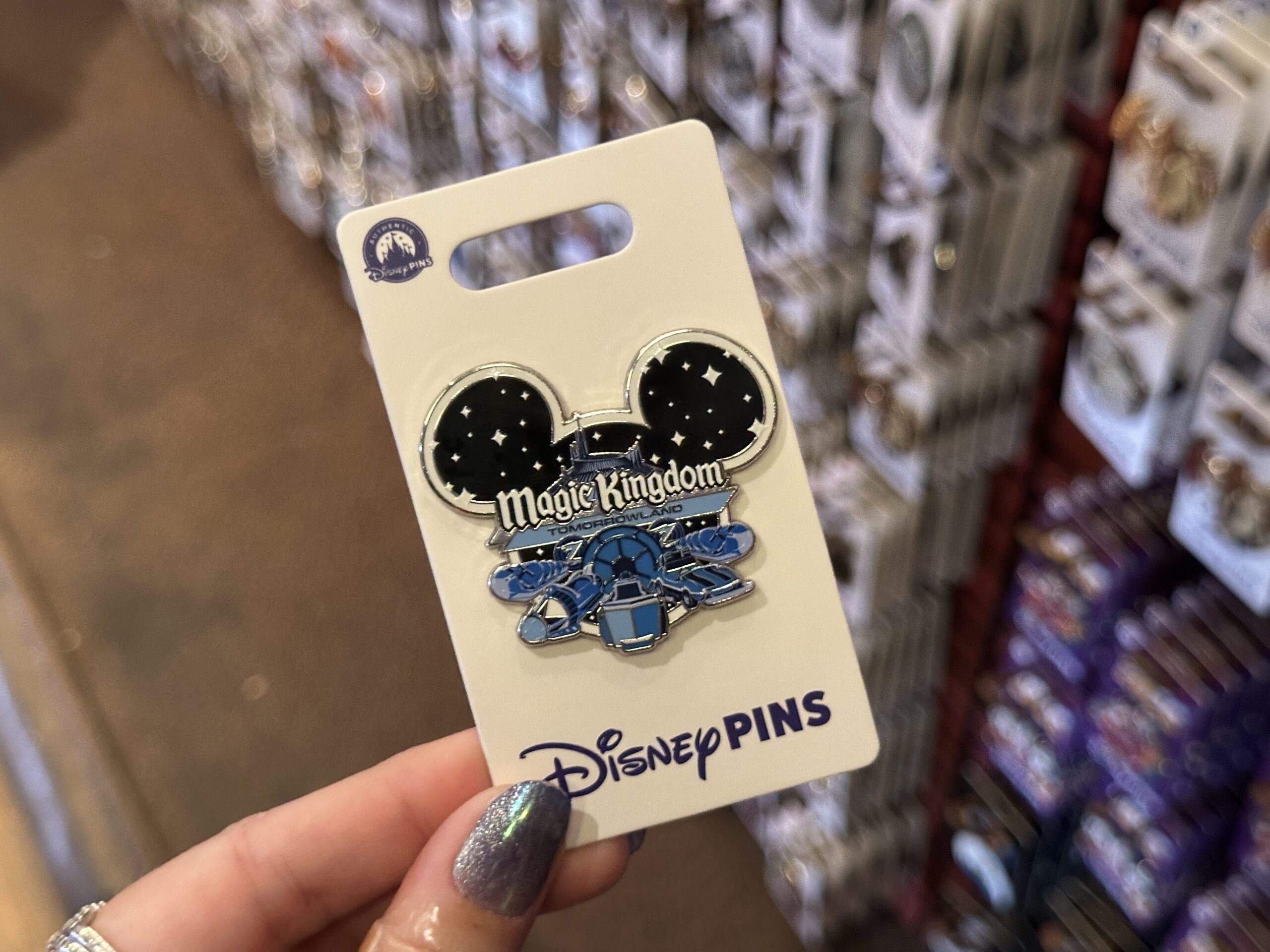 This Mickey-shaped pin includes the Magic Kingdom wordmark and "Tomorrowland" across the center. Behind the words is Space Mountain, set against a starry sky. In shades of blue across the bottom are ride vehicles from Tomorrowland attractions: Space Mountain, Astro Orbiter, Tomorrowland Speedway, and the PeopleMover.