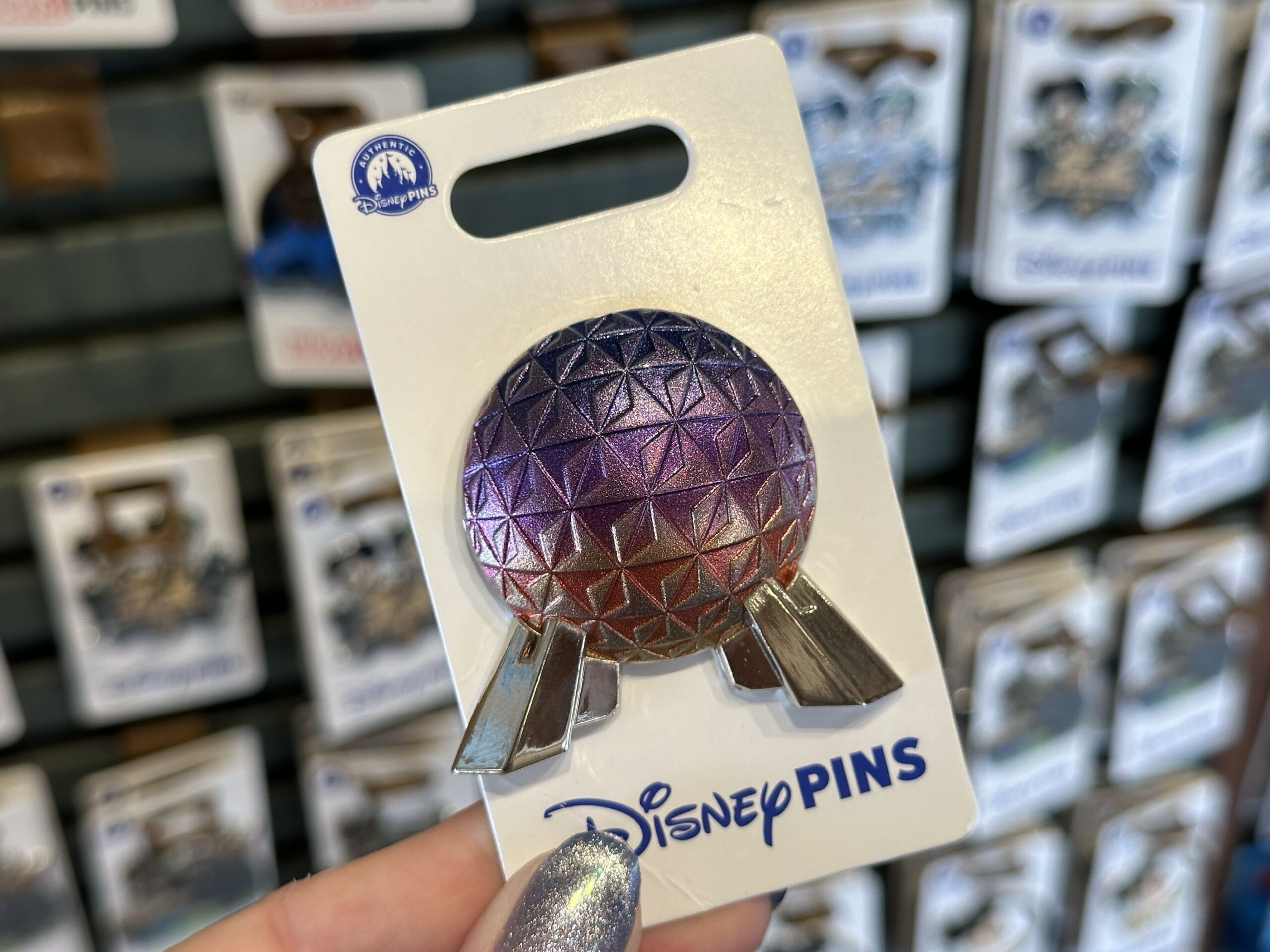 This Spaceship Earth pin has a textured surface with a blue-purple-orange gradient and sparkles based on the icon's light shows. Its legs are shiny silver.