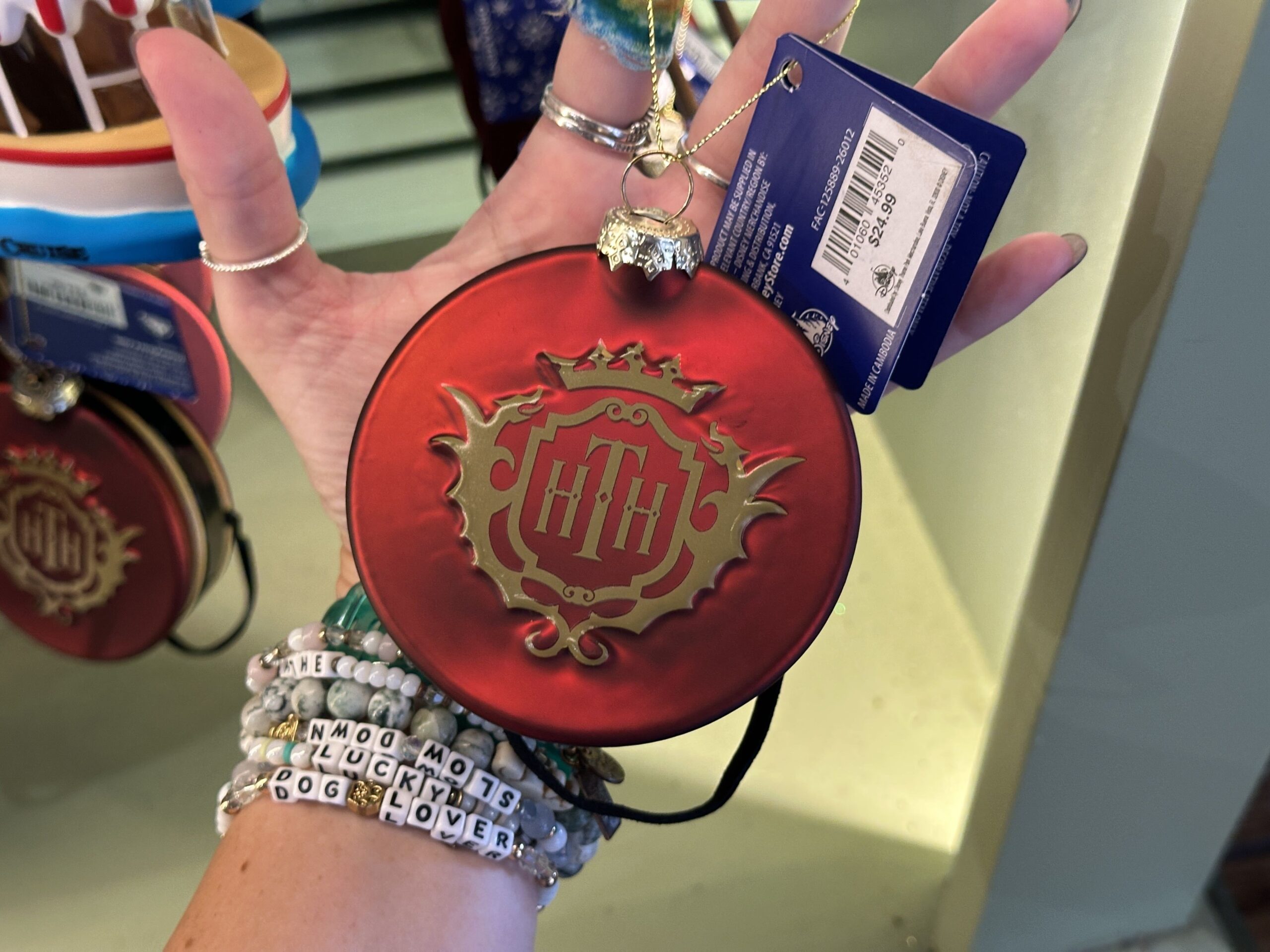 Based on the pillbox hats worn by The Twilight Zone Tower of Terror Cast Members, this red circular ornament has the Hollywood Tower Hotel logo in gold on top.