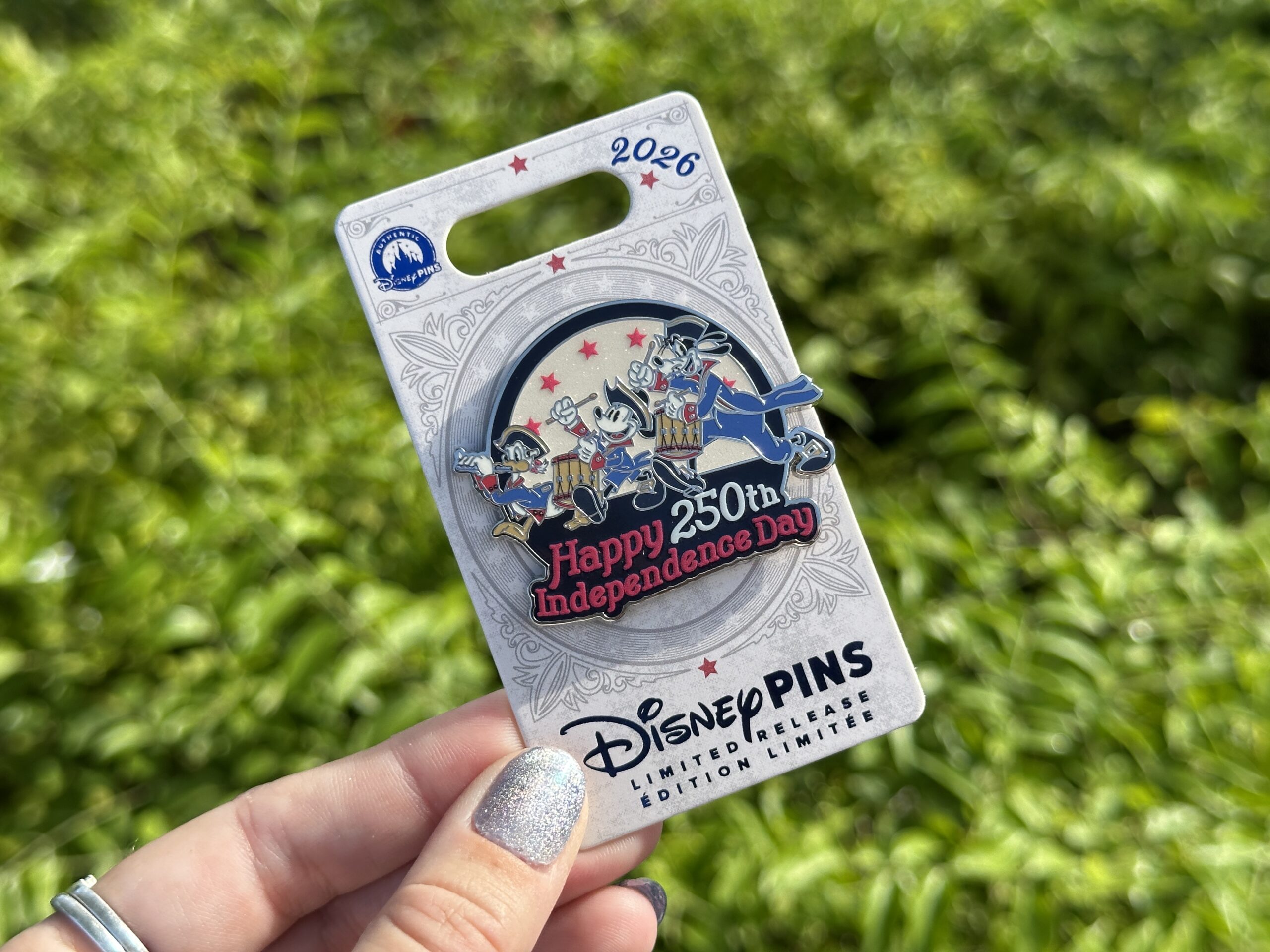 This limited release pin features Mickey Mouse, Donald Duck, and Goofy in red and blue uniforms similar to their Spirit of '76 costumes. Donald plays a flute while Mickey and Goofy march behind him on the drums. The background features red stars against a sparkly white circle.