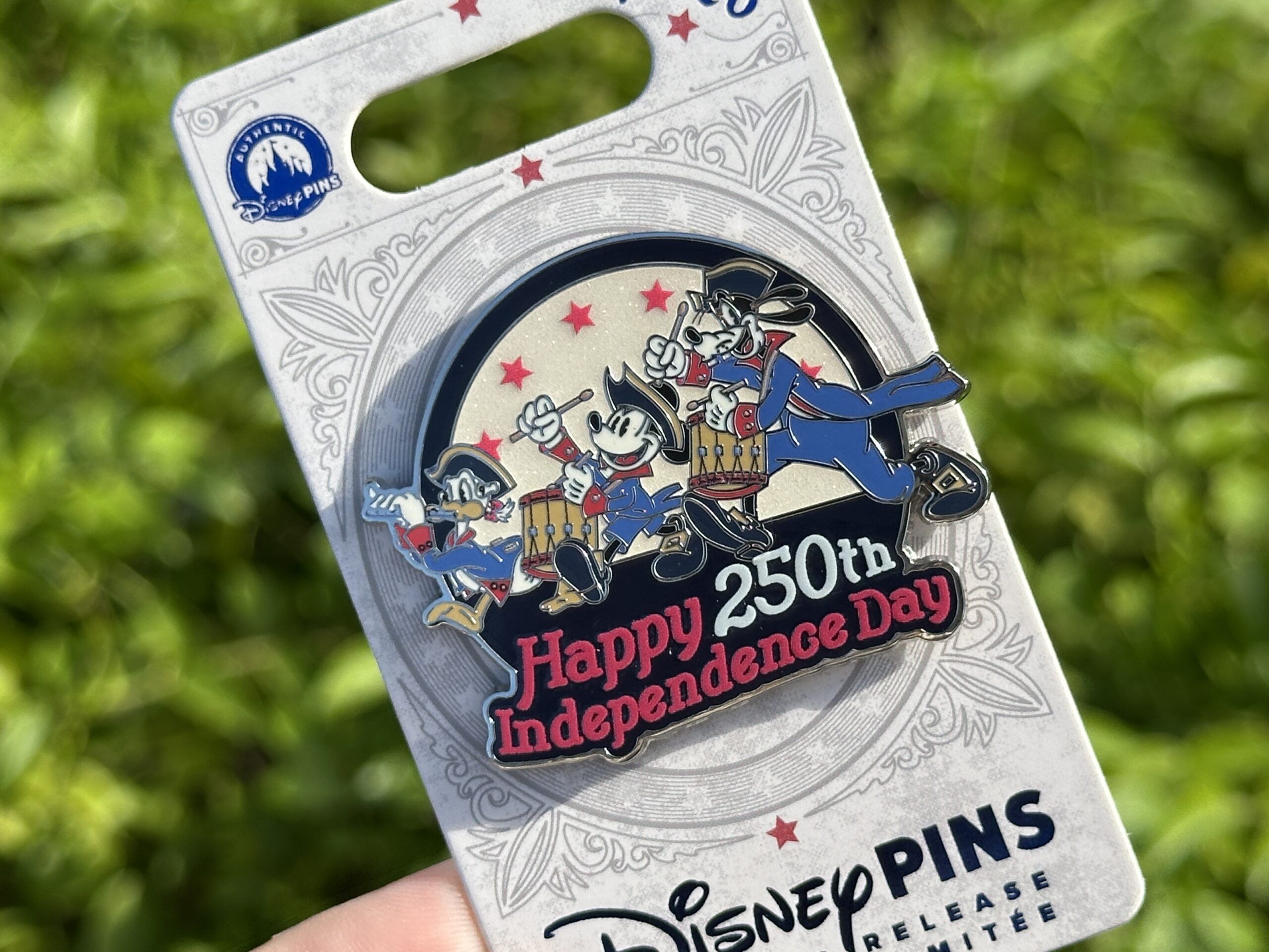 This limited release pin features Mickey Mouse, Donald Duck, and Goofy in red and blue uniforms similar to their Spirit of '76 costumes. Donald plays a flute while Mickey and Goofy march behind him on the drums. The background features red stars against a sparkly white circle.