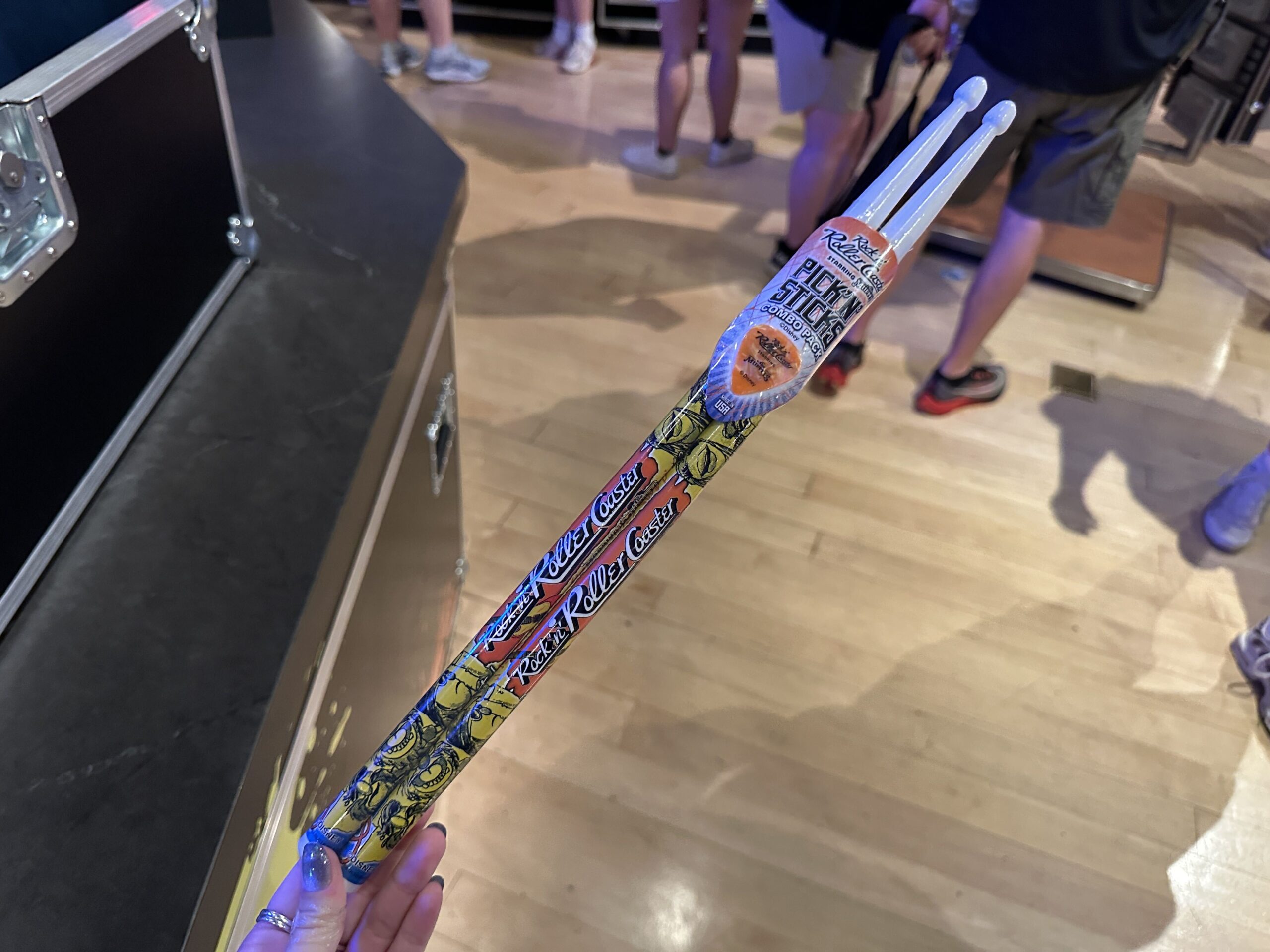 These drumsticks are mostly yellow on one side with white tips. "Rock 'n' Roller Coaster" is in white on an orange splotch in the center. The matching guitar pick is also orange with the Rock 'n' Roller Coaster Starring The Muppets wordmark.