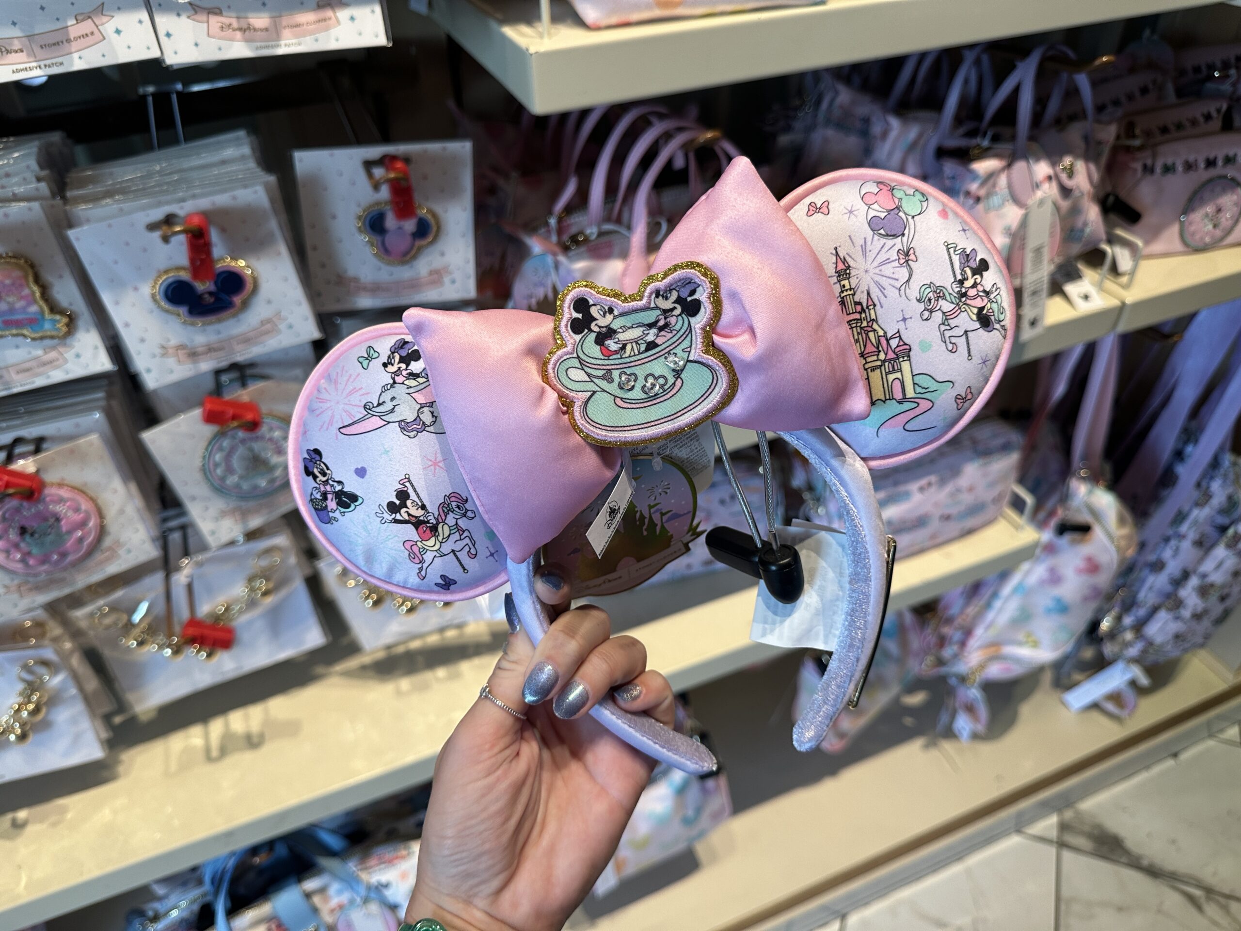 The ears feature images of Mickey and Minnie enjoying different Fantasyland rides including Dumbo the Flying Elephant and Prince Charming Regal Carrousel. Around them are hearts, bows, stars, fireworks, and balloons.